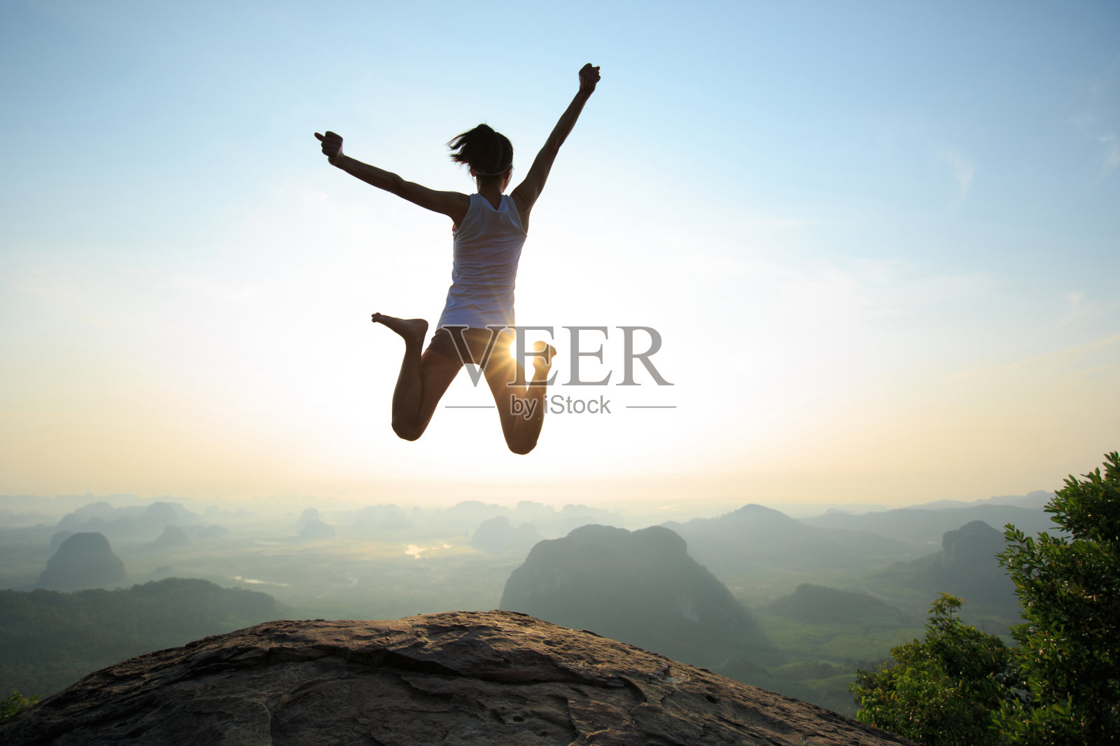 年轻女子跳跃在日出的落基山峰上，有自由、冒险、挑战、成功的观念照片摄影图片