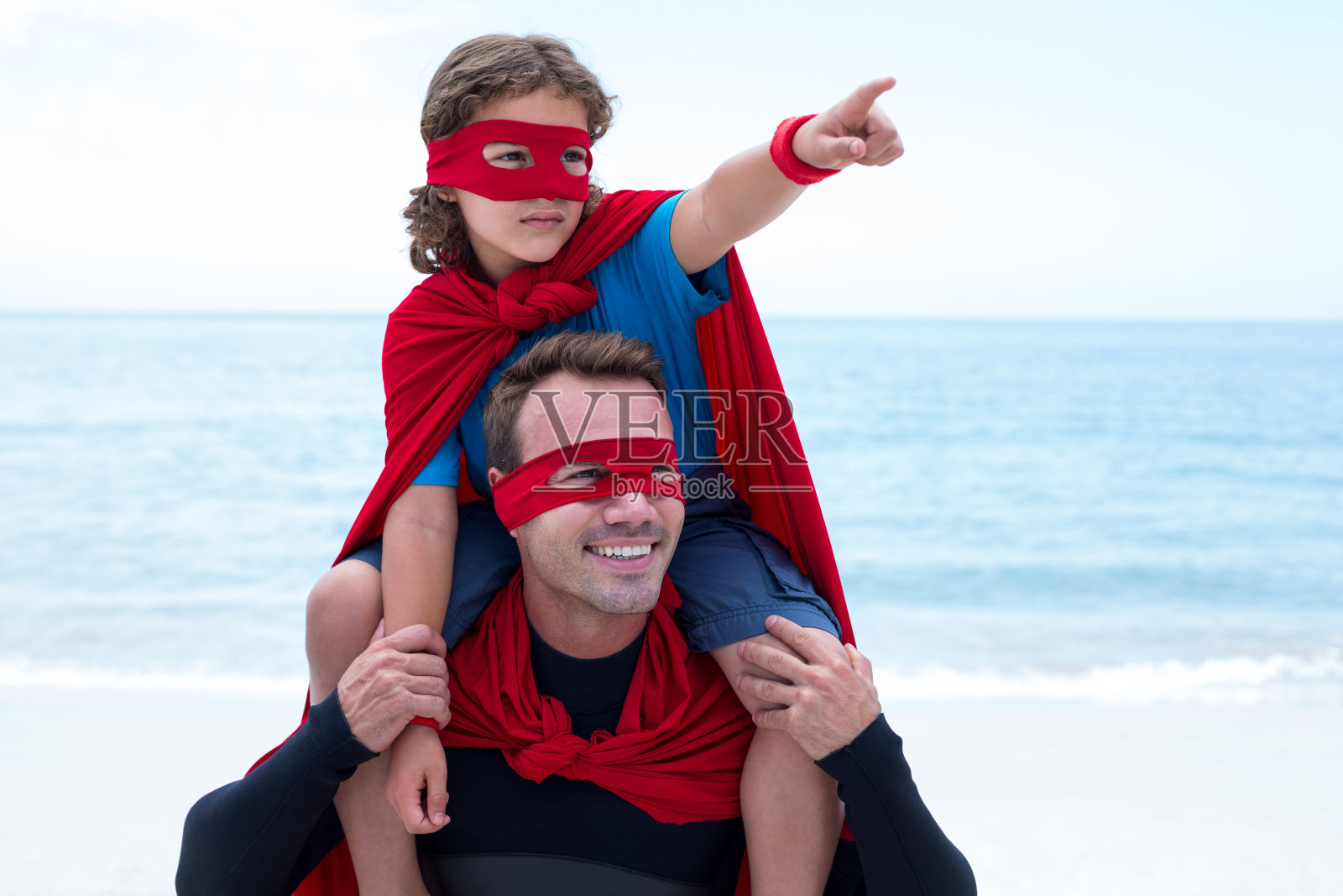 儿子穿着超级英雄服装指着父亲的肩膀照片摄影图片