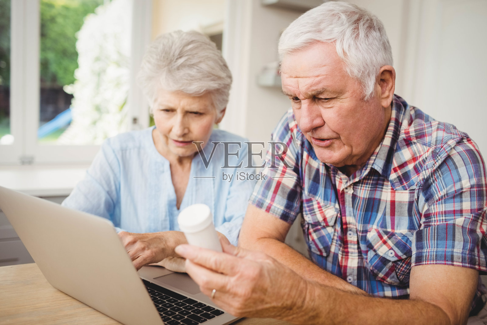 一对老年夫妇一边操作笔记本电脑一边拿着药瓶照片摄影图片