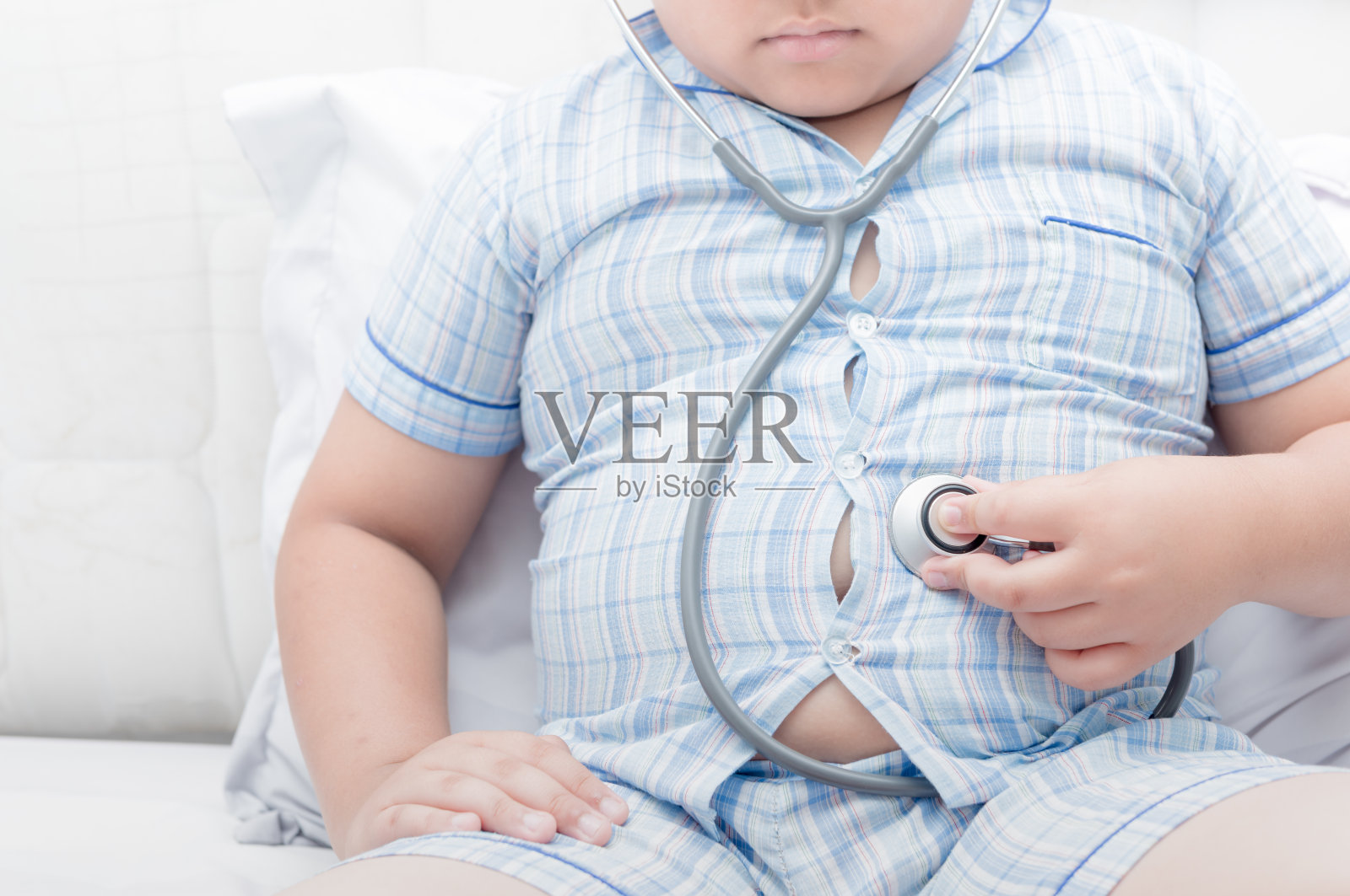 胖男孩用听诊器检查胃照片摄影图片