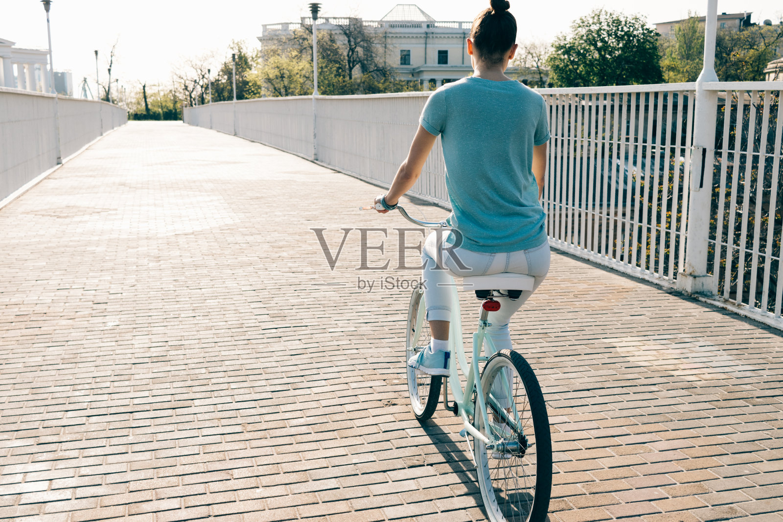 穿着牛仔裤和t恤的苗条女孩骑着一辆蓝色自行车穿过城市照片摄影图片
