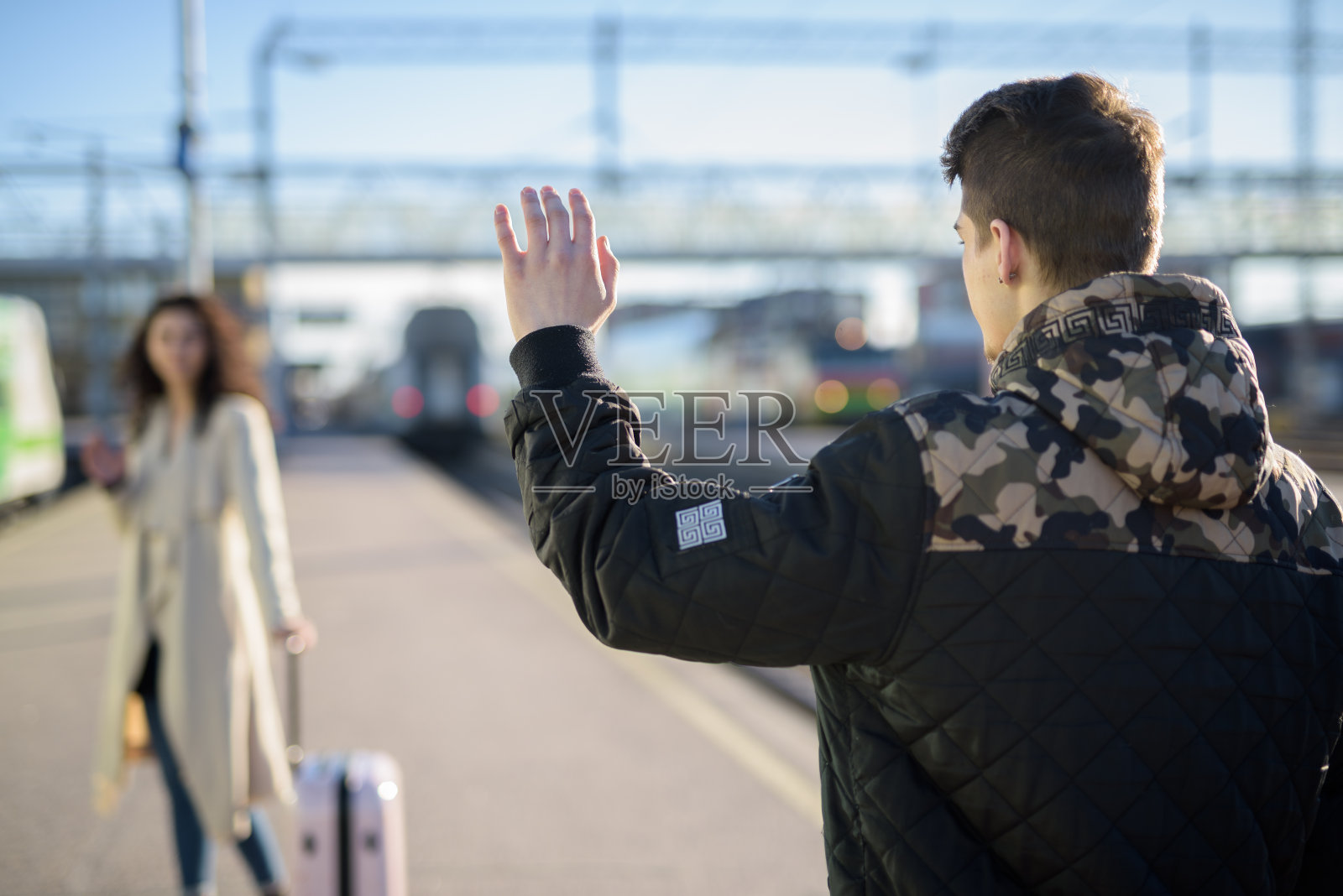 年轻的一对女子带着行李箱在火车站站台离开，男友挥手告别照片摄影图片