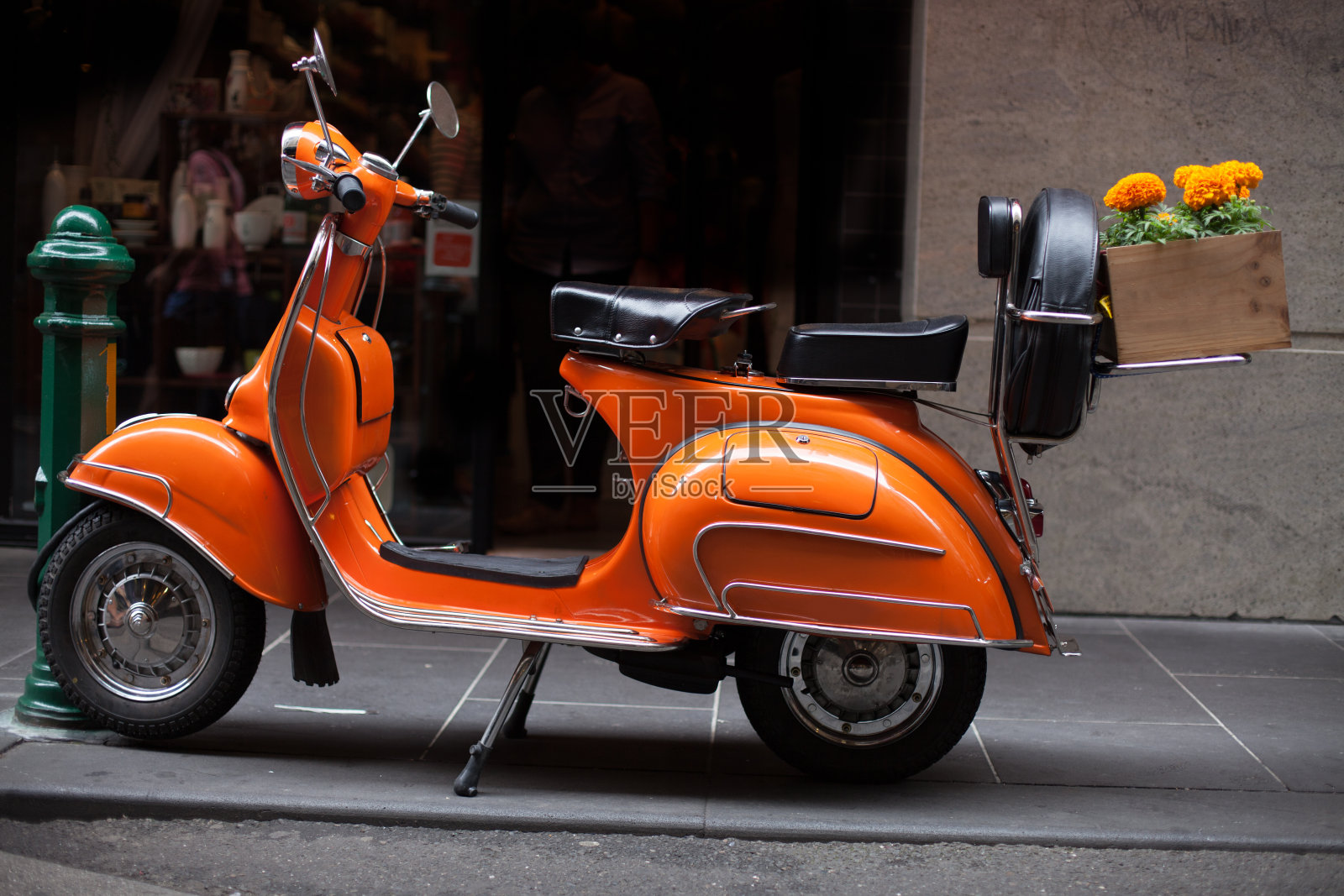 一辆橙色踏板车停在墨尔本大街上，木制的箱子里装着橙色万寿菊。照片摄影图片