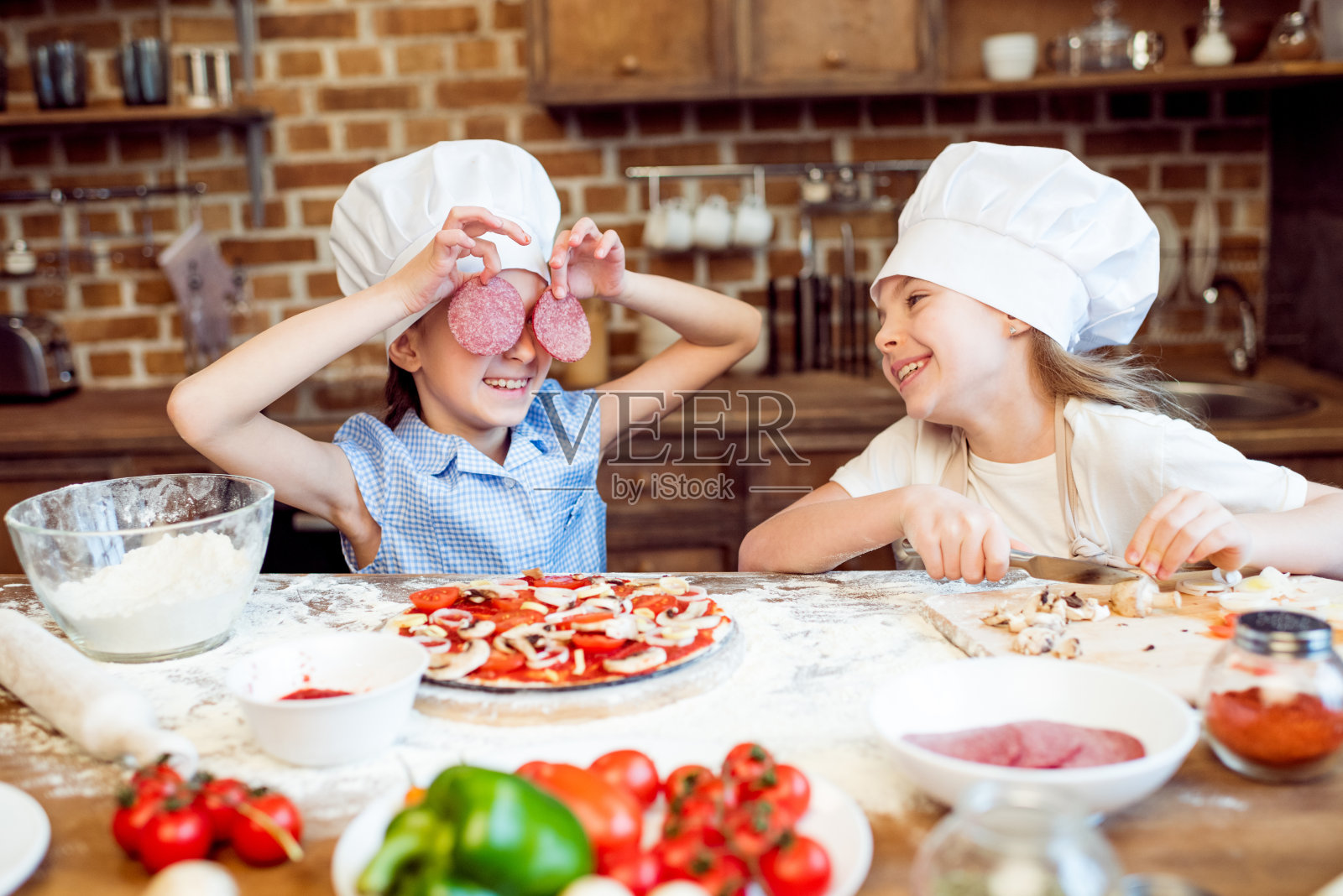 戴着厨师帽的孩子们在做披萨的时候玩得很开心照片摄影图片