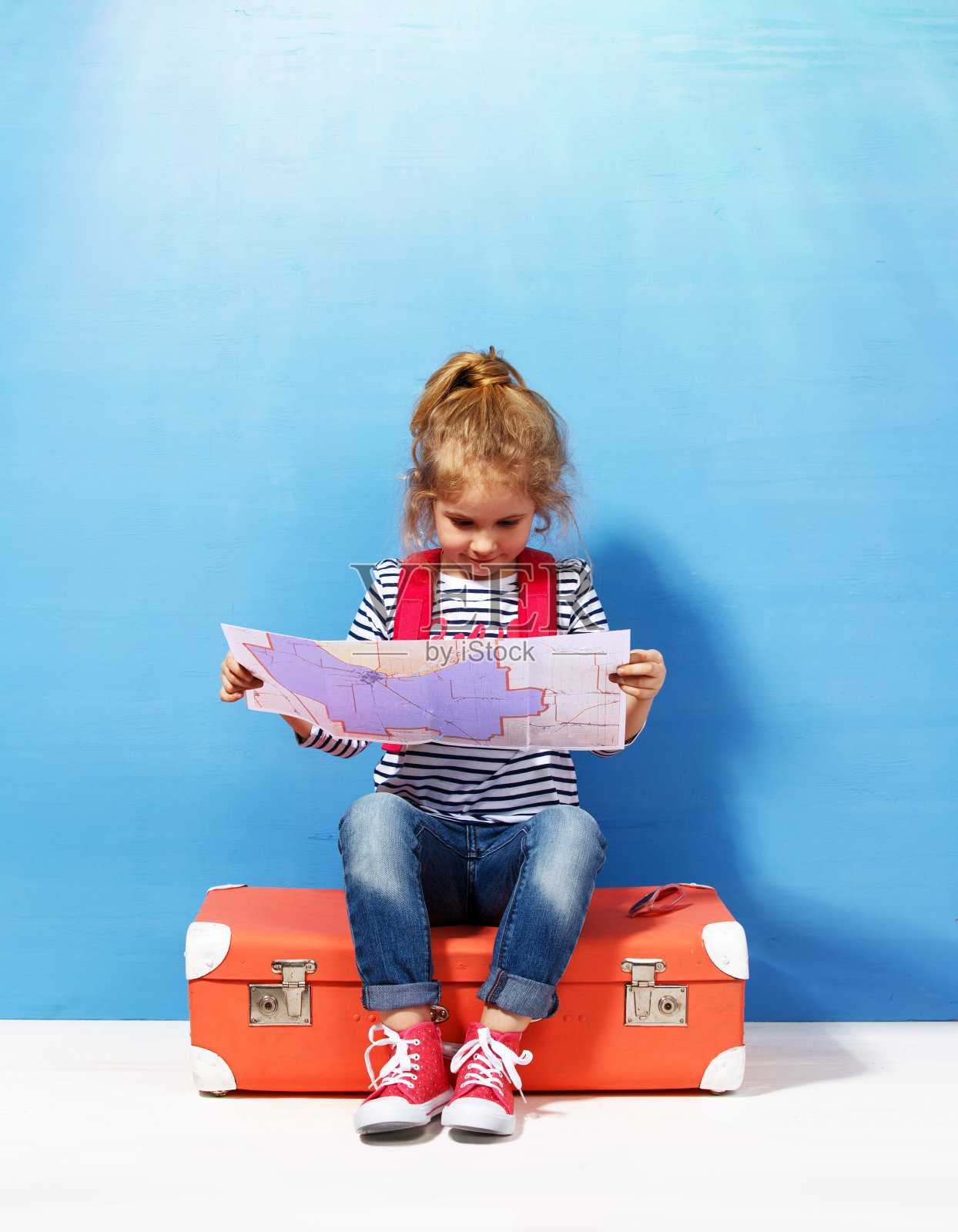 金发碧眼的小女孩带着粉色的复古行李箱和城市地图准备迎接暑假。旅行和冒险概念照片摄影图片