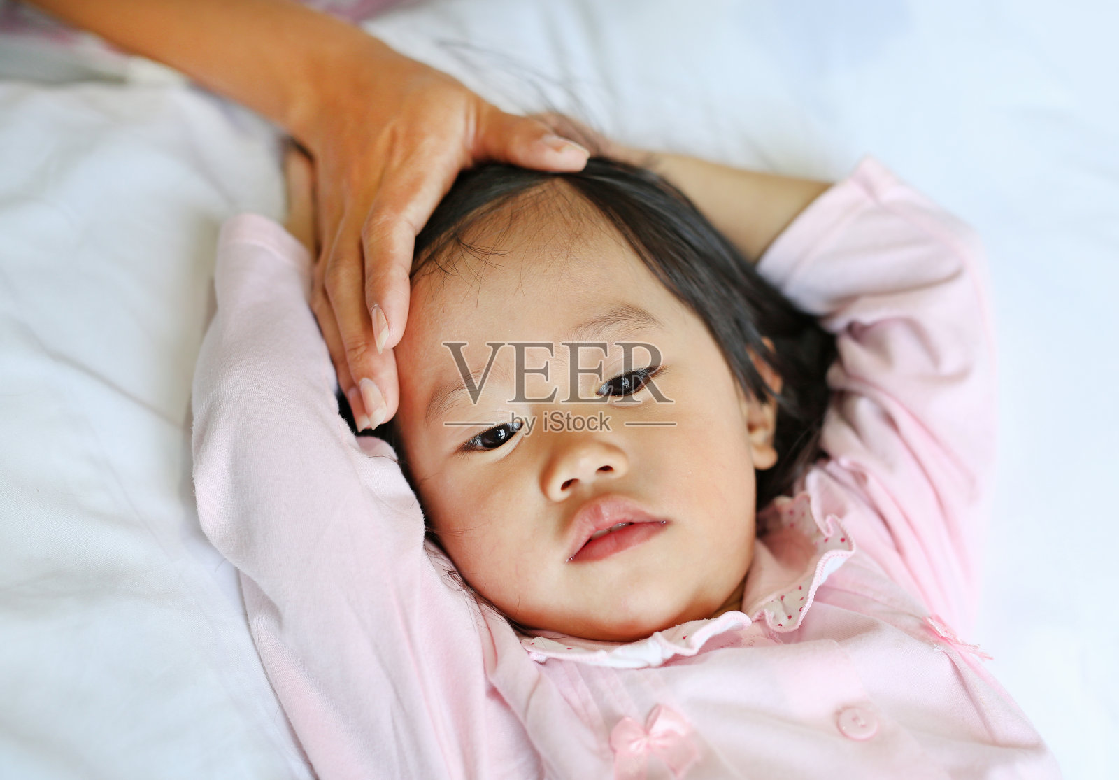 生病的女孩躺在床上用手摸着妈妈的头。照片摄影图片