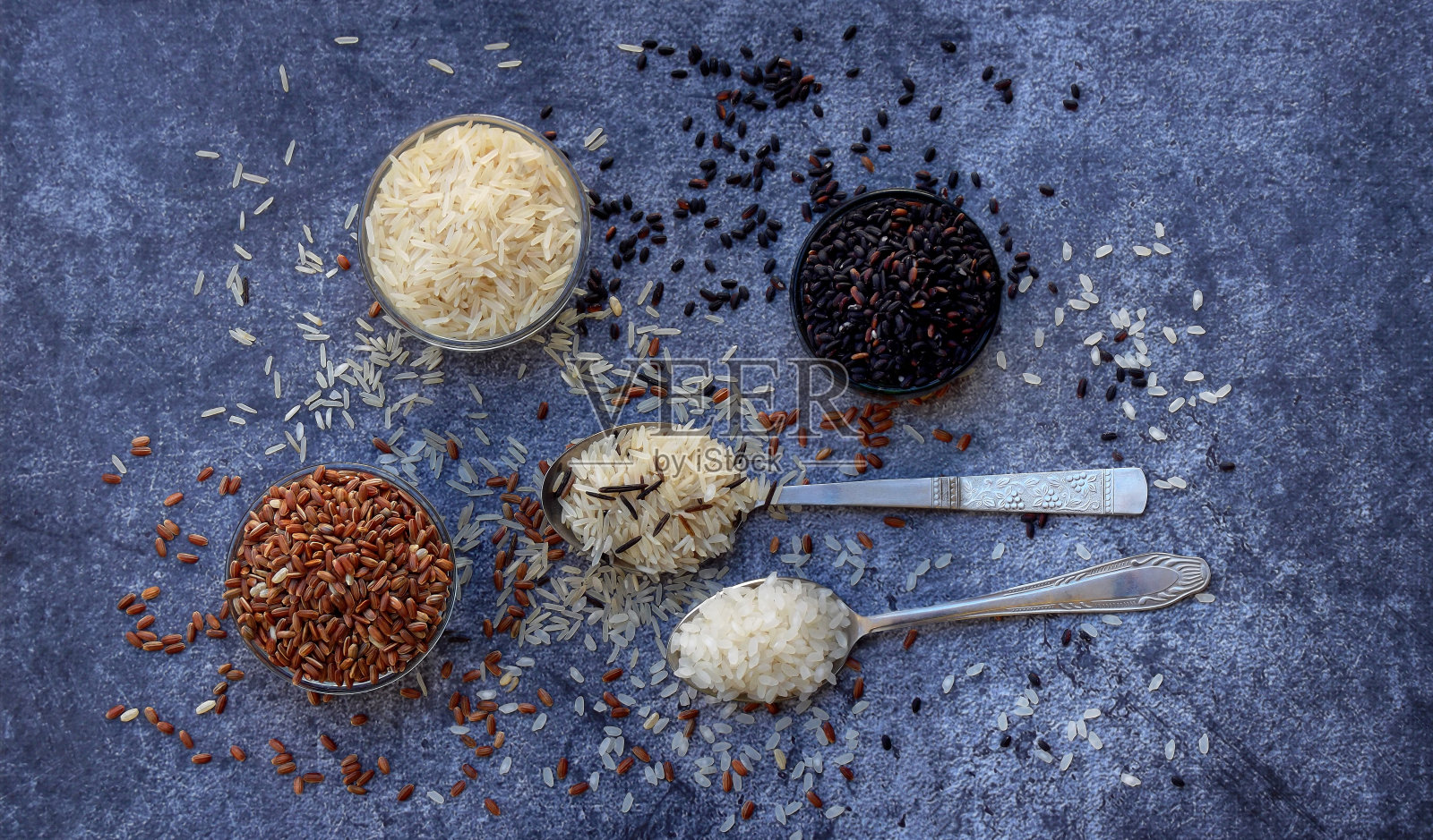 不同类型的大米在灰色的背景:白色糯米，黑色，印度香米，棕色和混合大米。健康的概念。前视图。副本的空间。照片摄影图片
