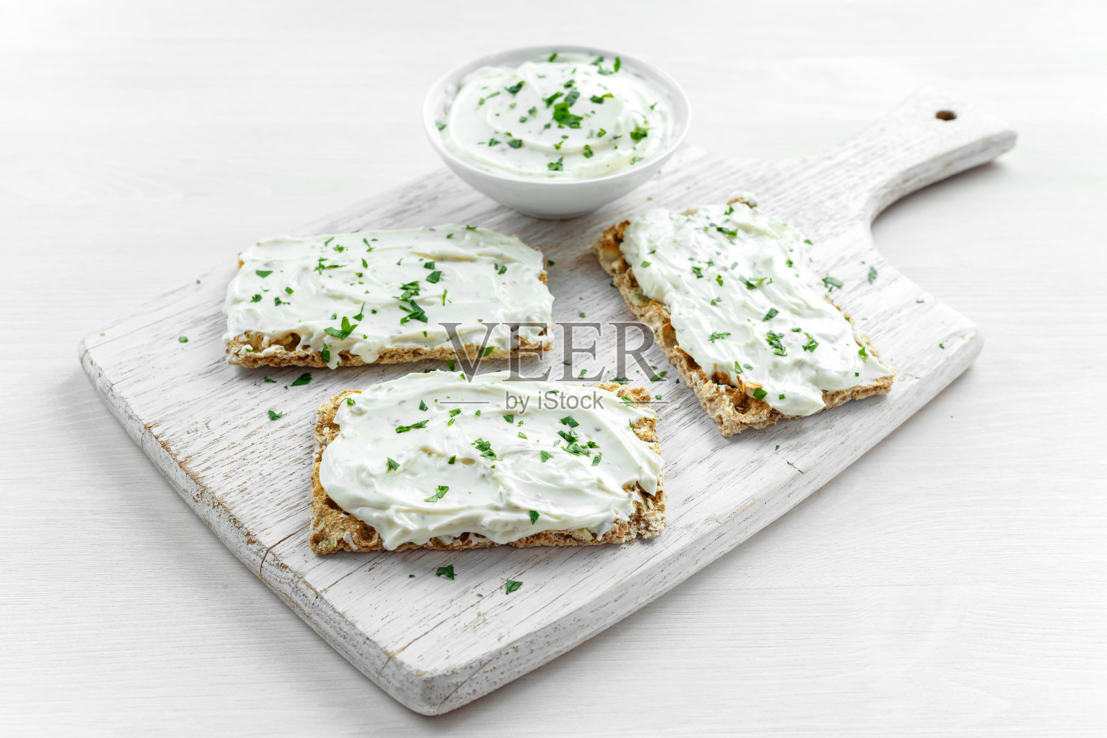 自制脆饼吐司配奶油芝士和欧芹在白色木板背景上。照片摄影图片
