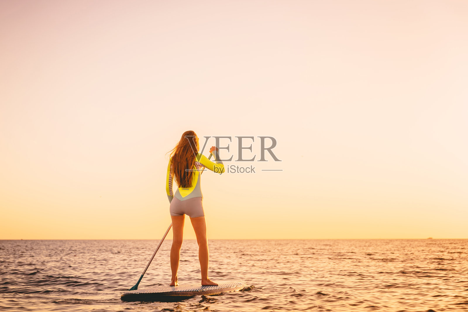 苗条的年轻女子站起来划桨板与美丽的日落或日出的颜色照片摄影图片