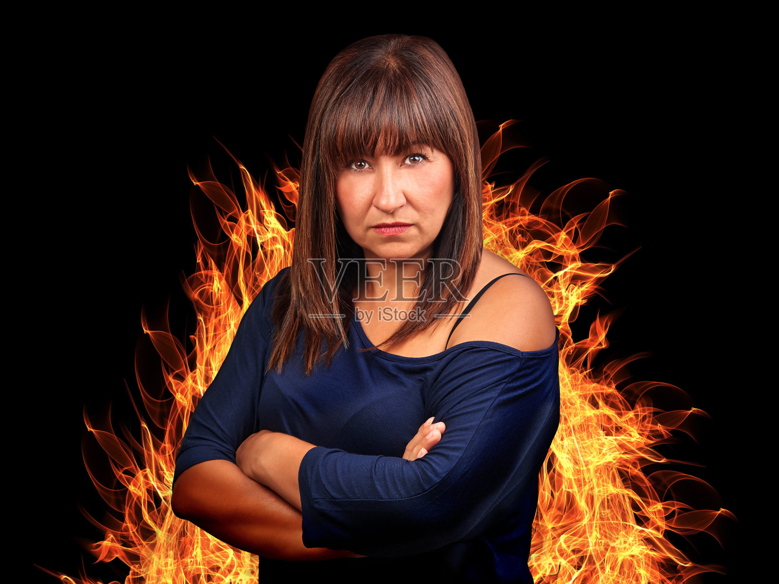 黑发女人愤怒地交叉双臂，被火包围照片摄影图片