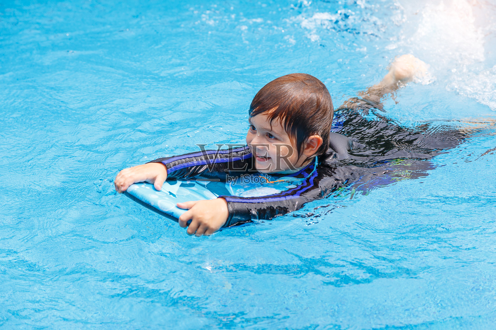 小男孩在学游泳池游泳，用泡沫垫练习照片摄影图片