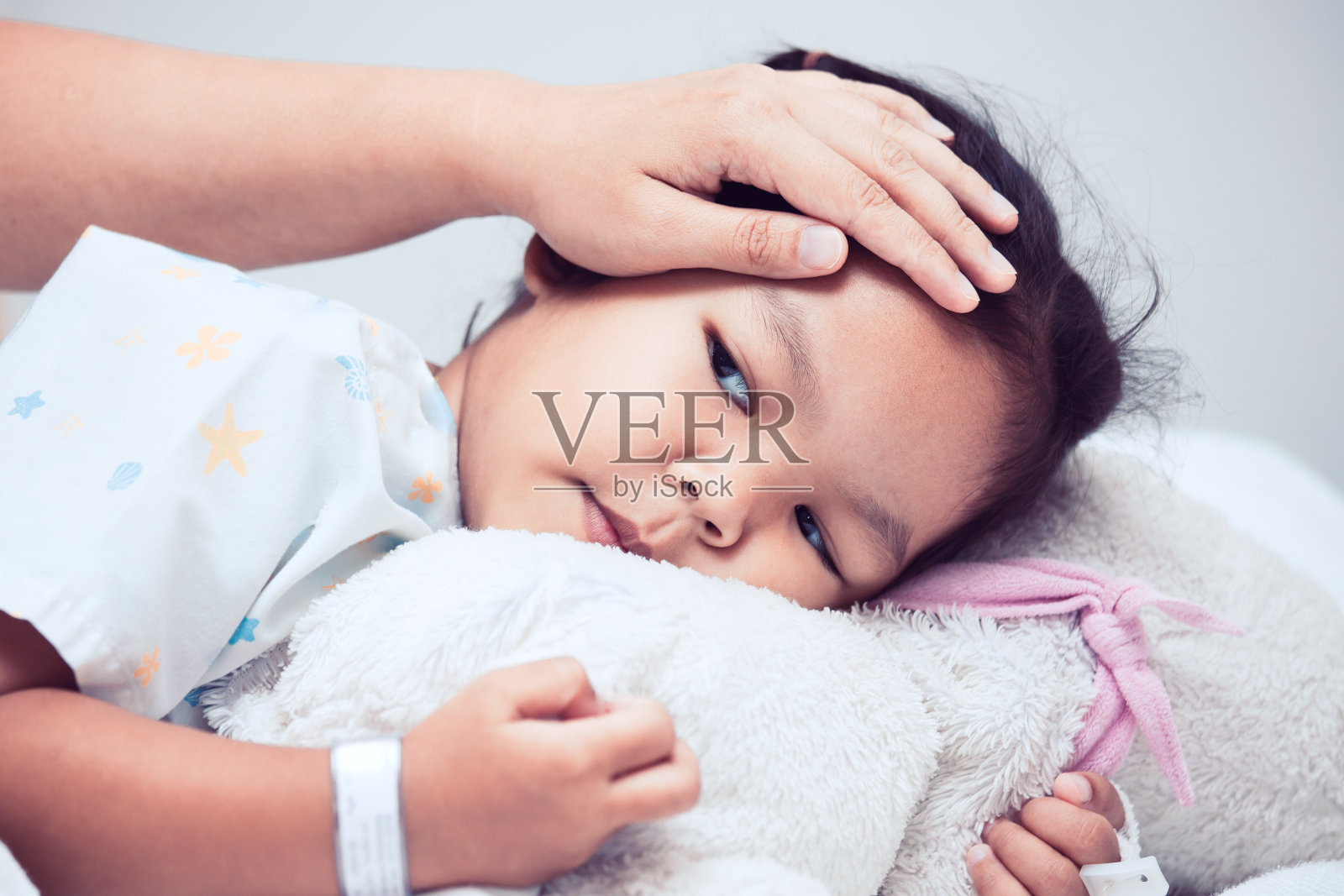生病的亚洲女孩躺在床上，母亲用手抚摸着她的额头照片摄影图片