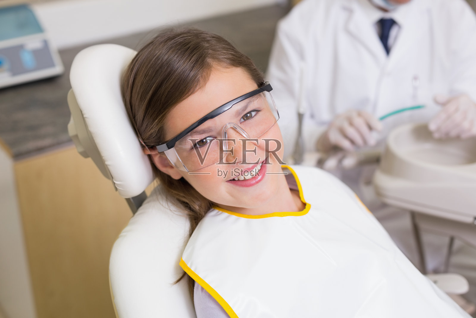 小女孩坐在牙医的椅子上戴着防护眼镜照片摄影图片