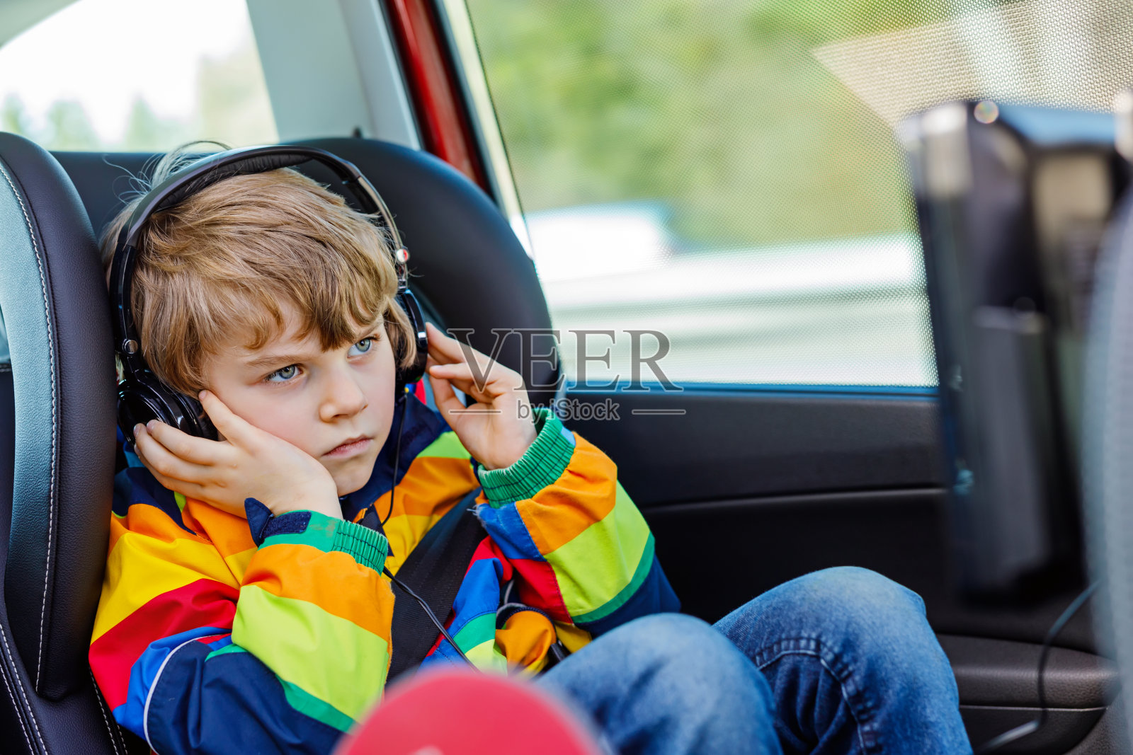 金发小男孩在长途汽车驾驶中戴着耳机看电视或dvd照片摄影图片