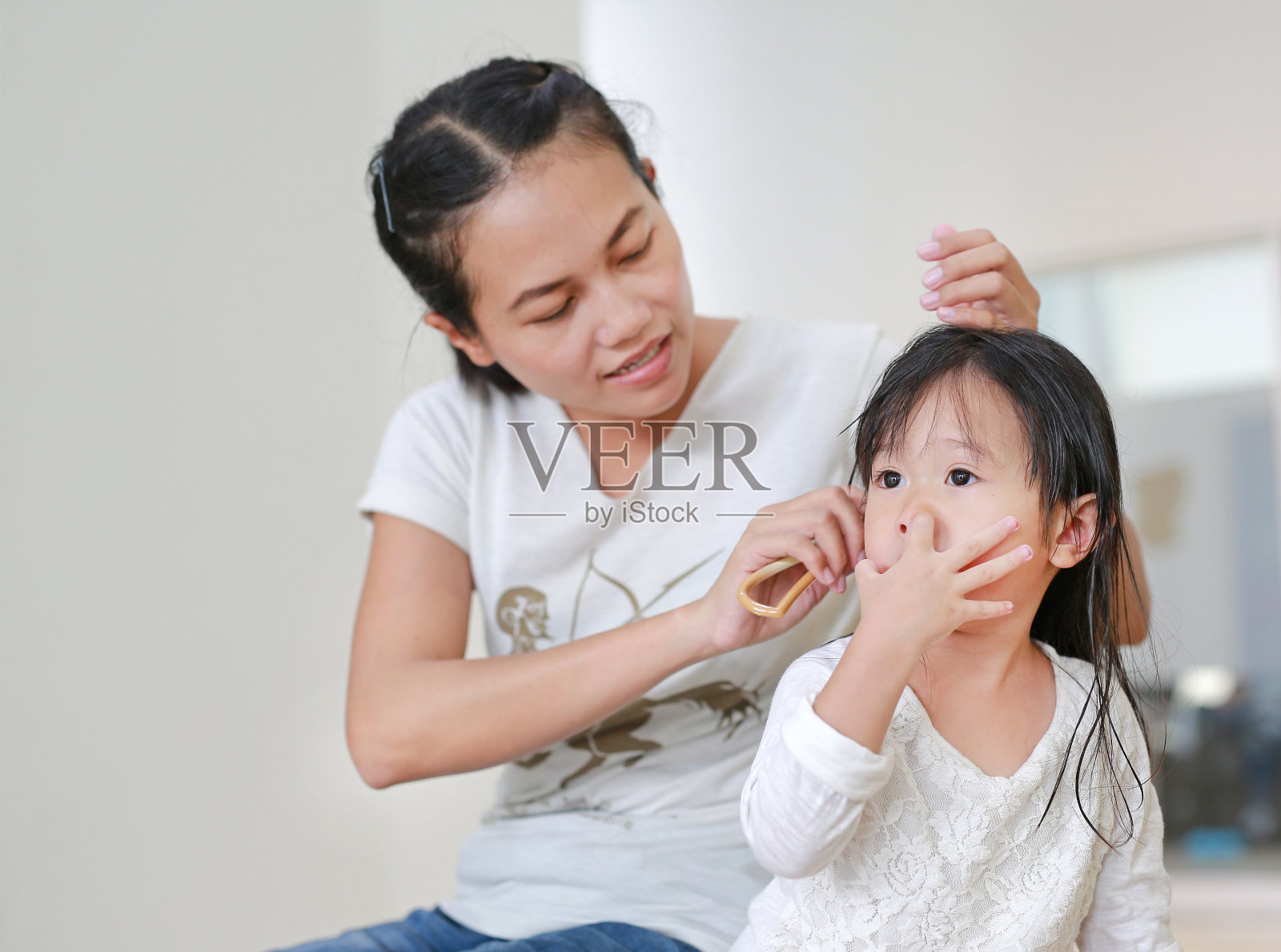 宝宝洗浴后，妈妈正在用女儿滑稽的脸给女儿梳头。照片摄影图片