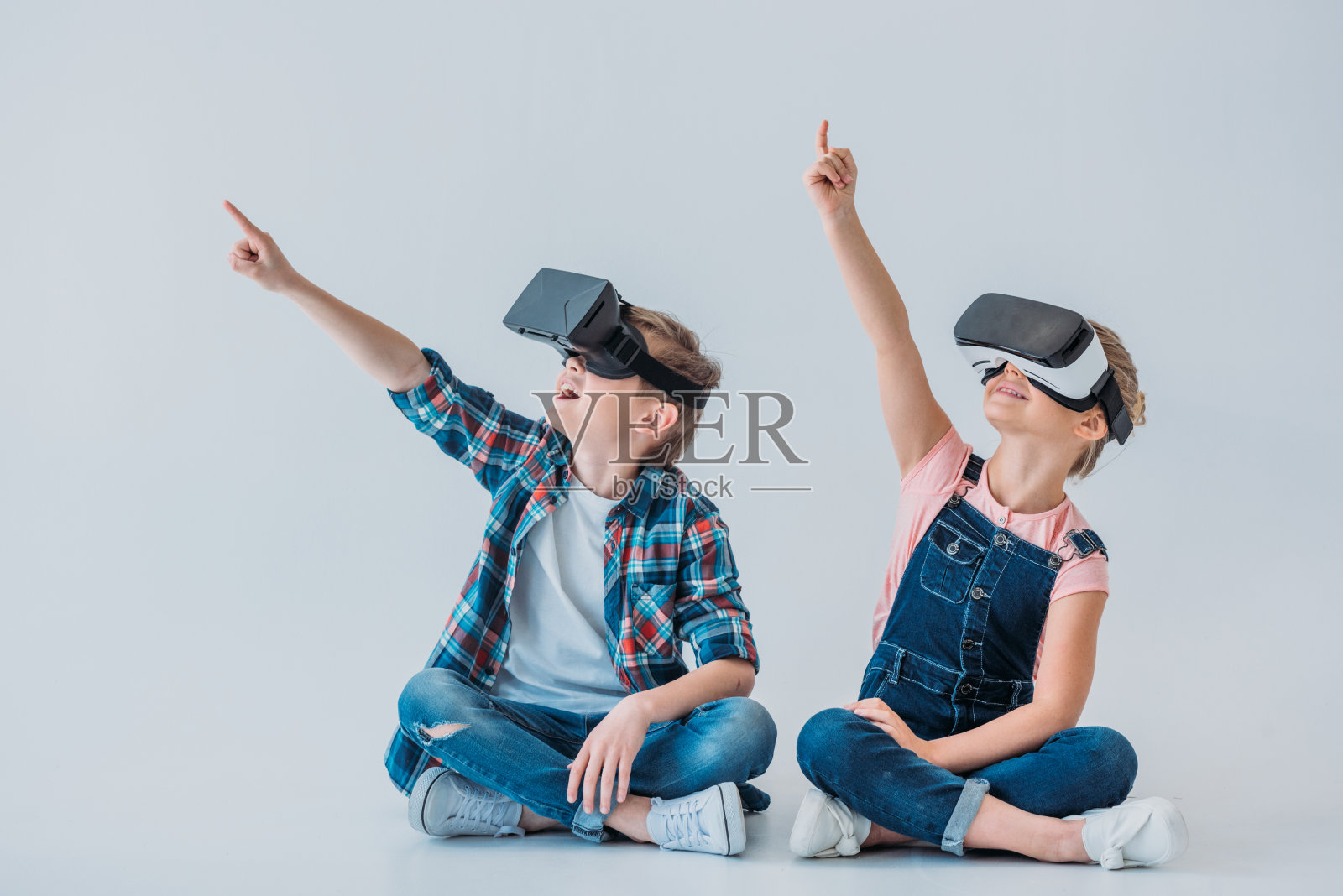 孩子们戴着虚拟现实耳机，坐在地板上用手指向上指照片摄影图片