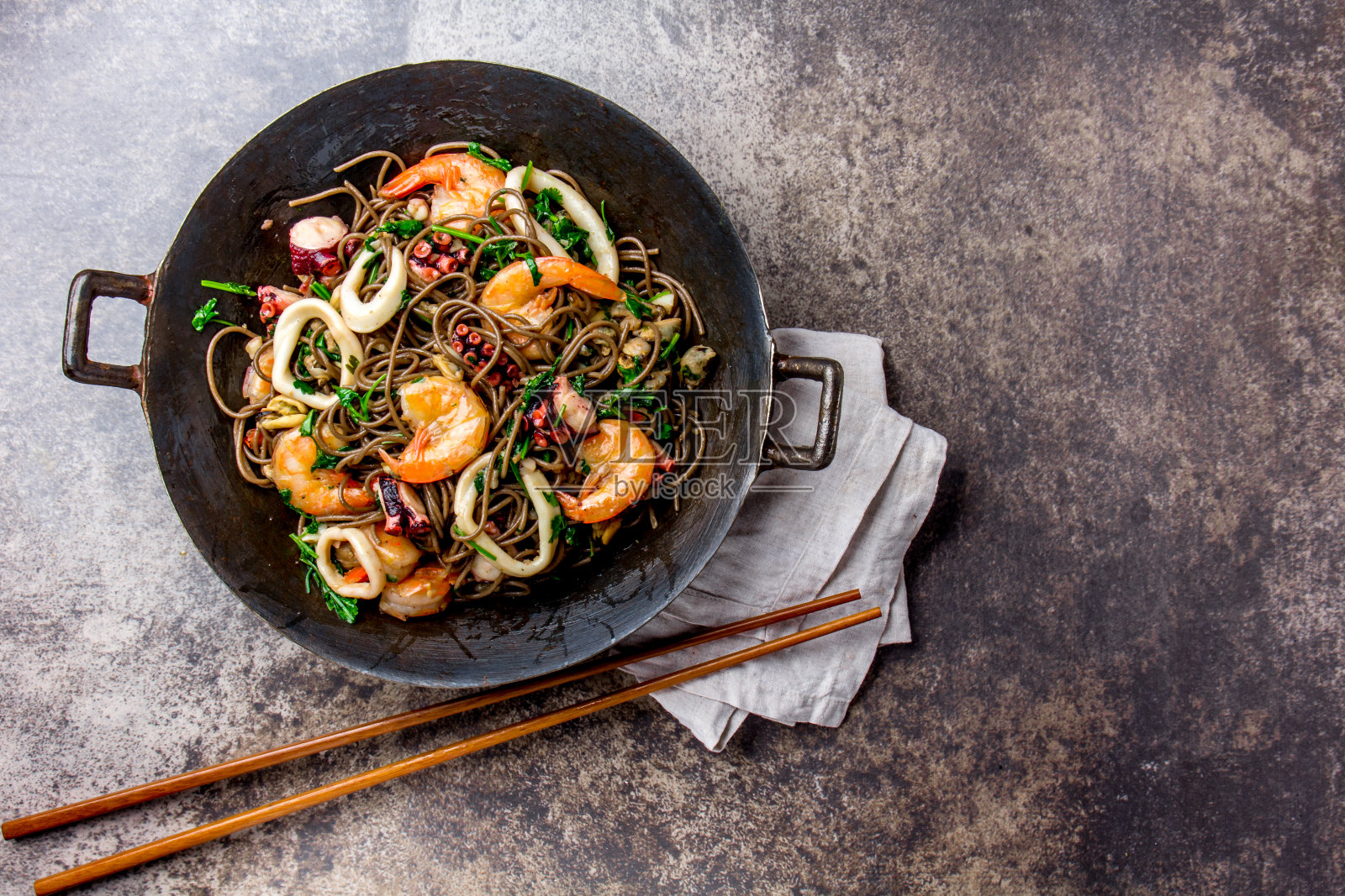 荞麦炒面海鲜-虾，章鱼，鱿鱼在铸铁亚洲炒锅与烹饪筷子。俯视图，石头背景照片摄影图片