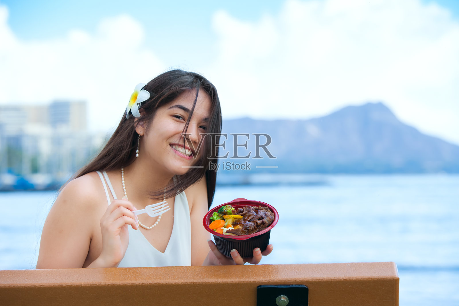 混血年轻女子在吃夏威夷烧烤，背景是钻石头照片摄影图片
