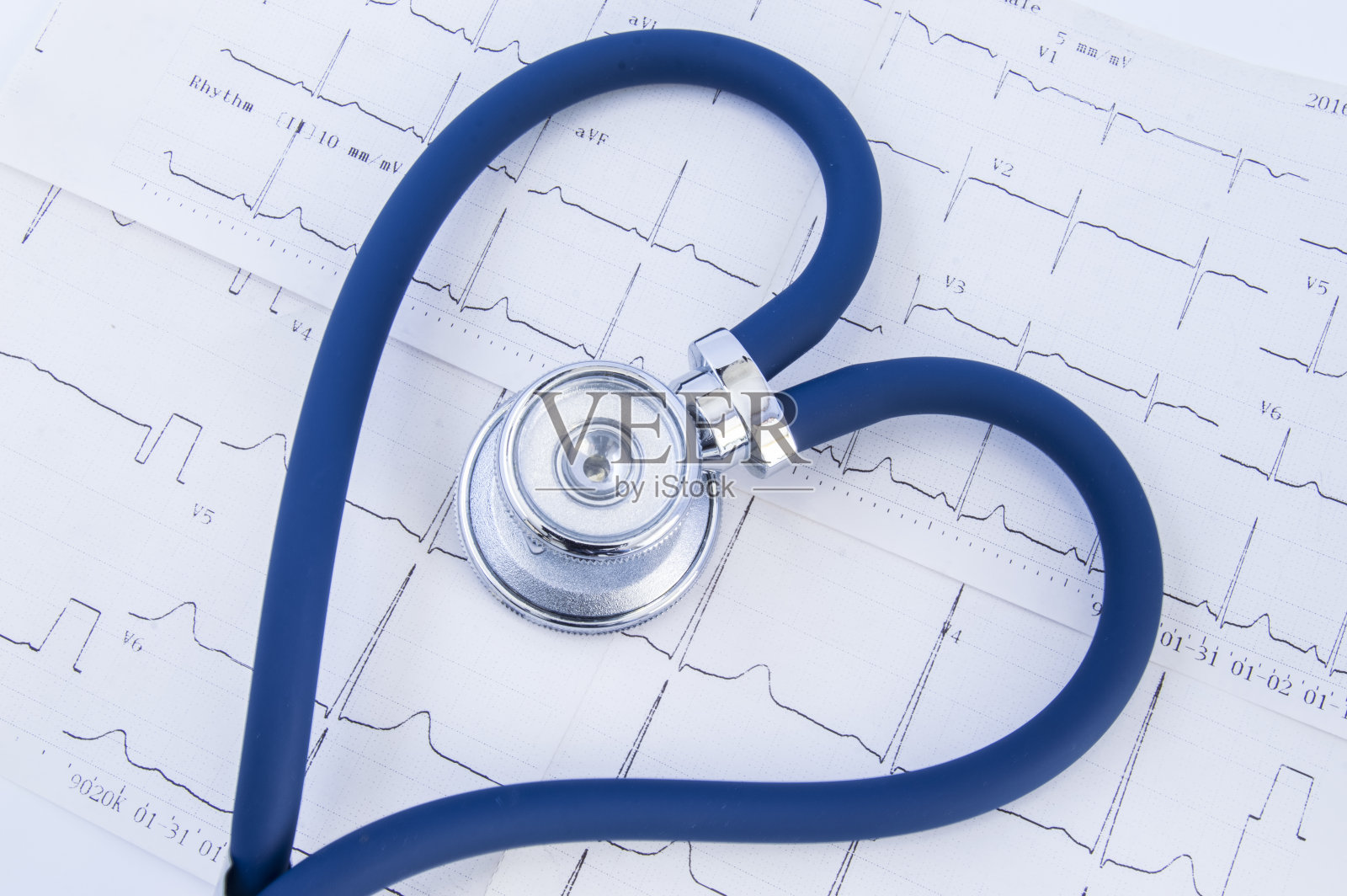 心脏成形听诊器以心电图为背景。头部或胸部和蓝色听诊器的柔性管折叠成心脏形状，躺在打印的心电图上照片摄影图片