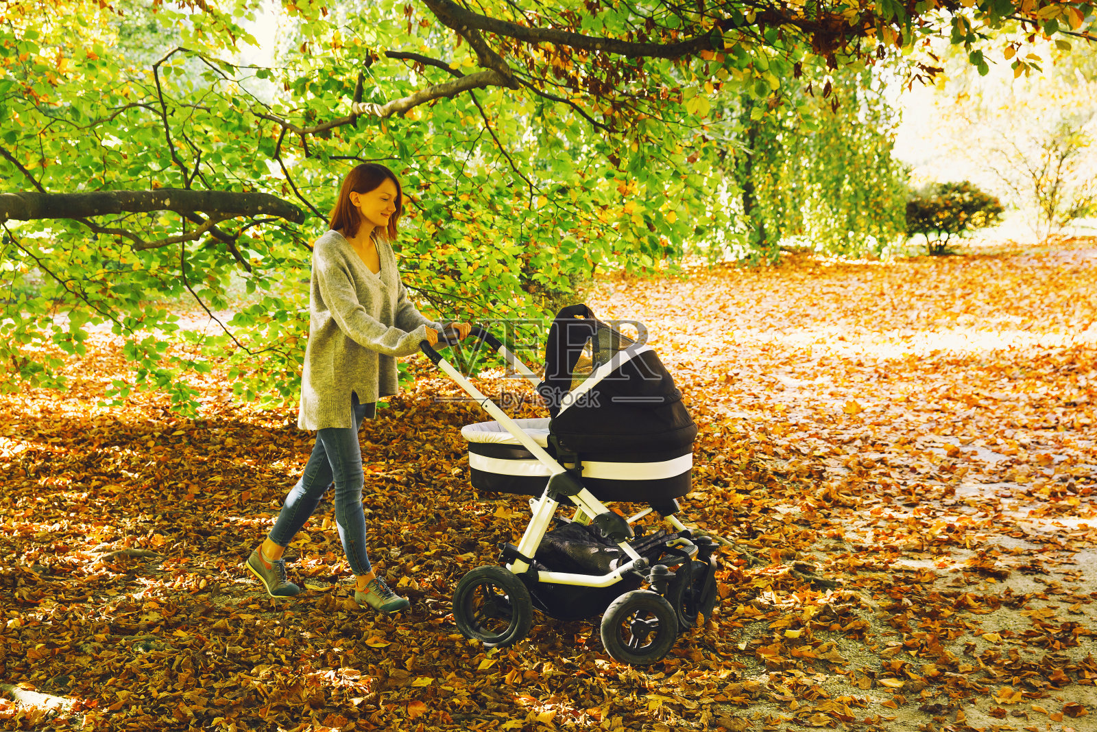 美丽的年轻母亲与婴儿车散步在秋天的公园。照片摄影图片