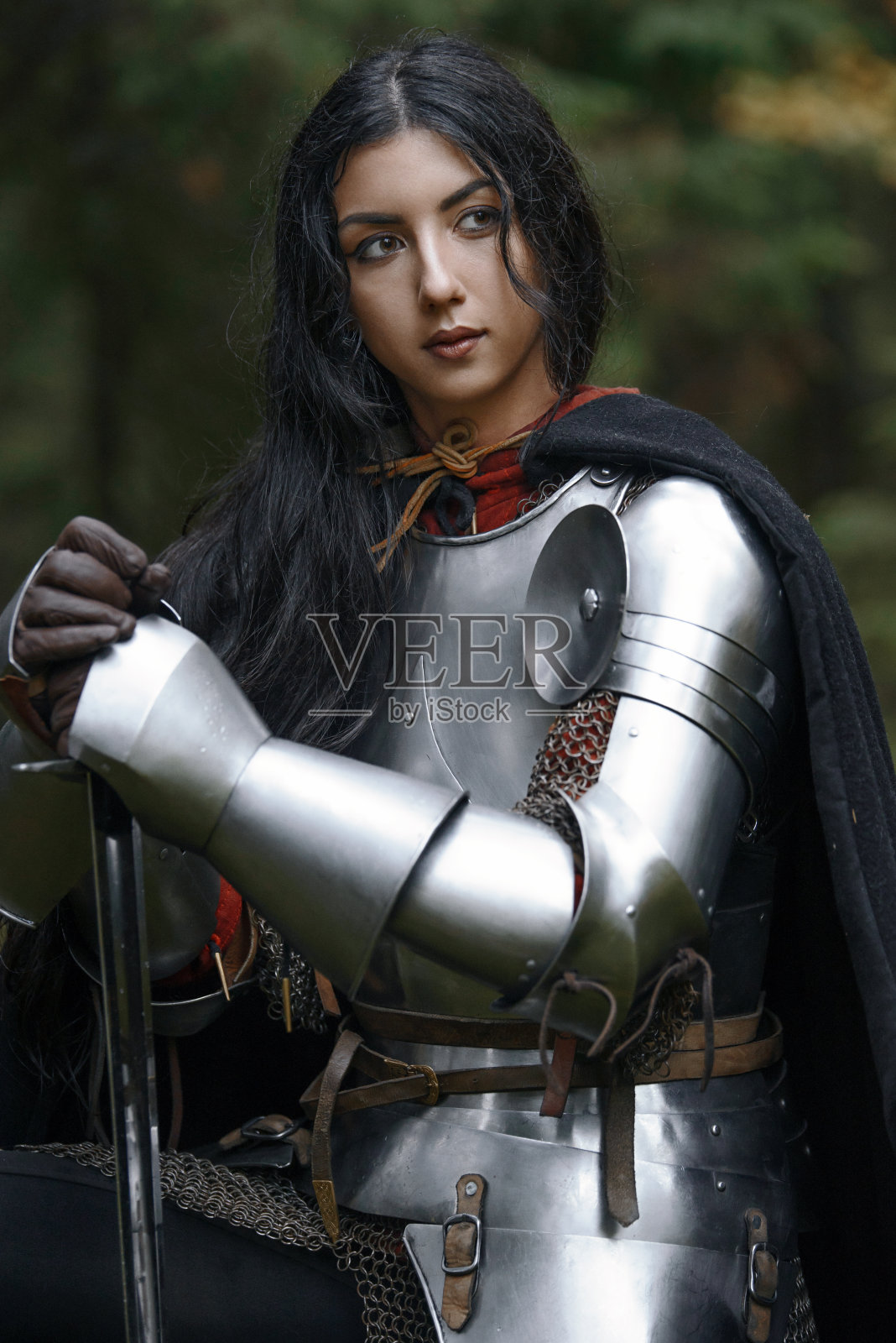 一个美丽的战士女孩带着剑，穿着链甲和盔甲在一个神秘的森林。照片摄影图片