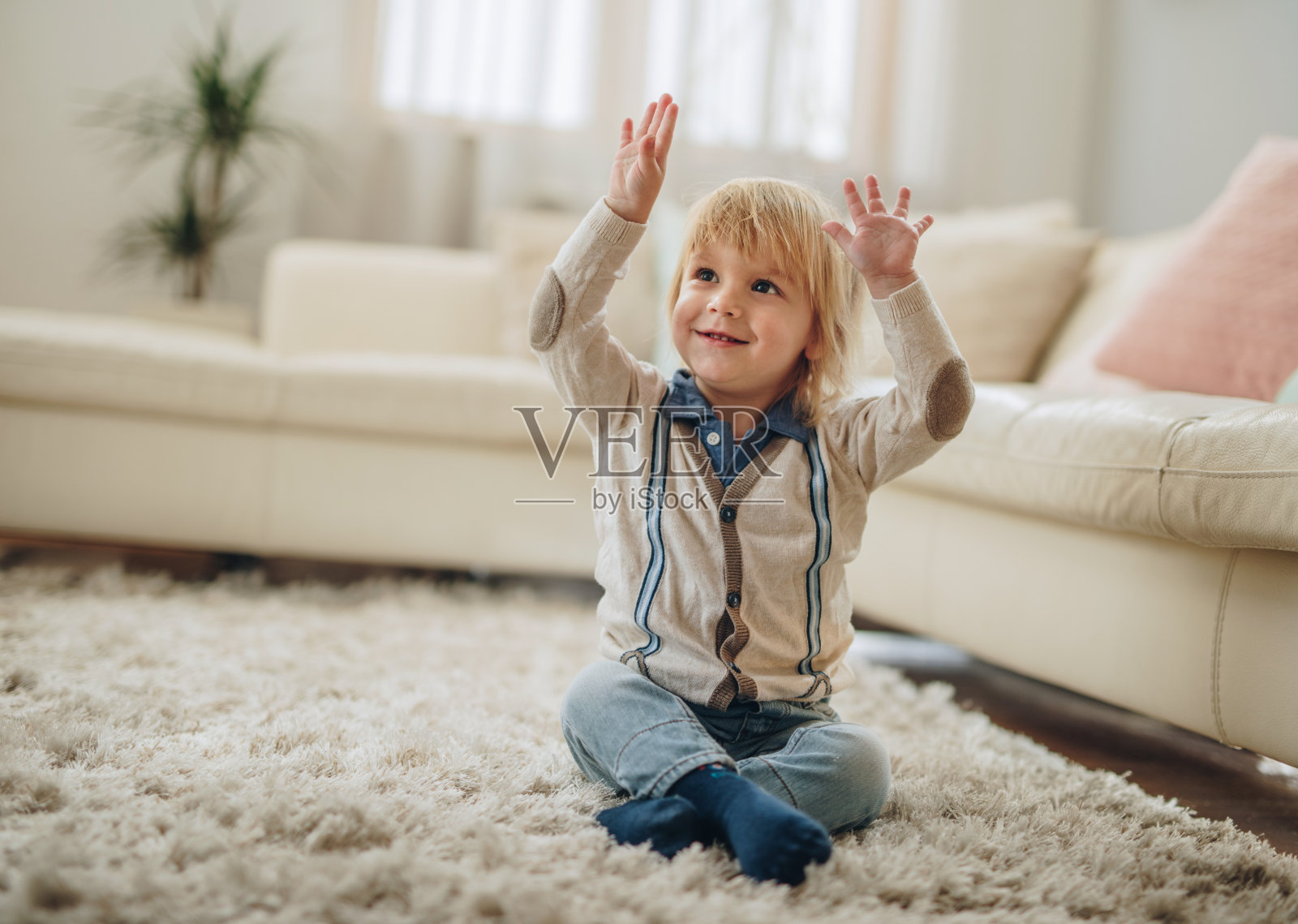 无忧无虑的小男孩在家里的地毯上放松地举起双臂。照片摄影图片