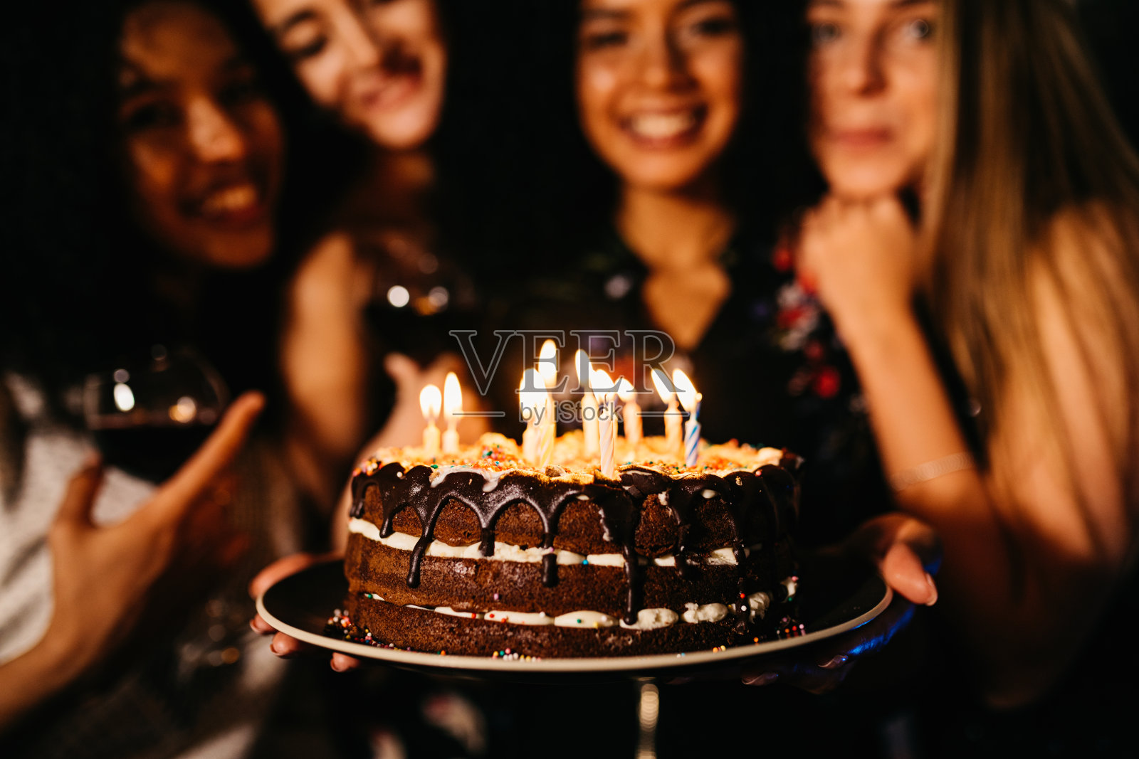 女人拿着生日蛋糕和朋友站在室内的特写镜头照片摄影图片