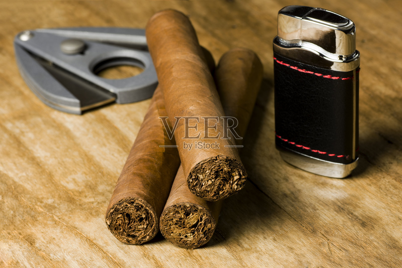 三支古巴雪茄，一个打火机和一个切刀放在一张旧木板桌上照片摄影图片