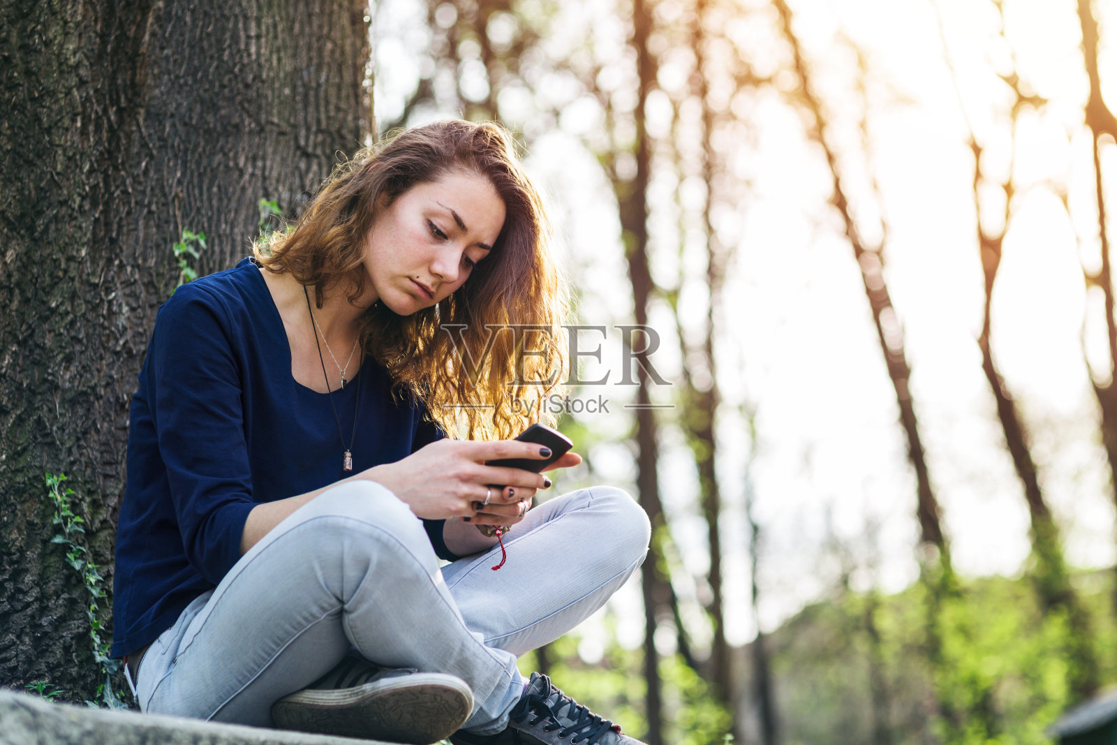 一个少女在公园里用手机发短信。照片摄影图片