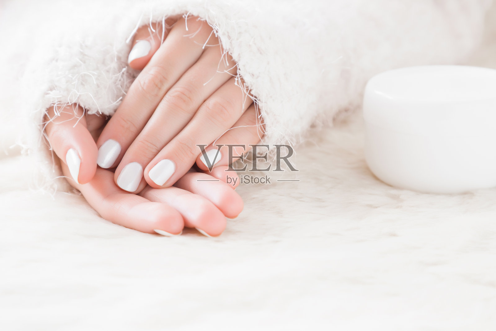 漂亮整洁的女人的手和奶油罐在蓬松的毯子上。冬季清洁柔软肌肤的保湿霜。修指甲美容院。医疗保健的概念。照片摄影图片