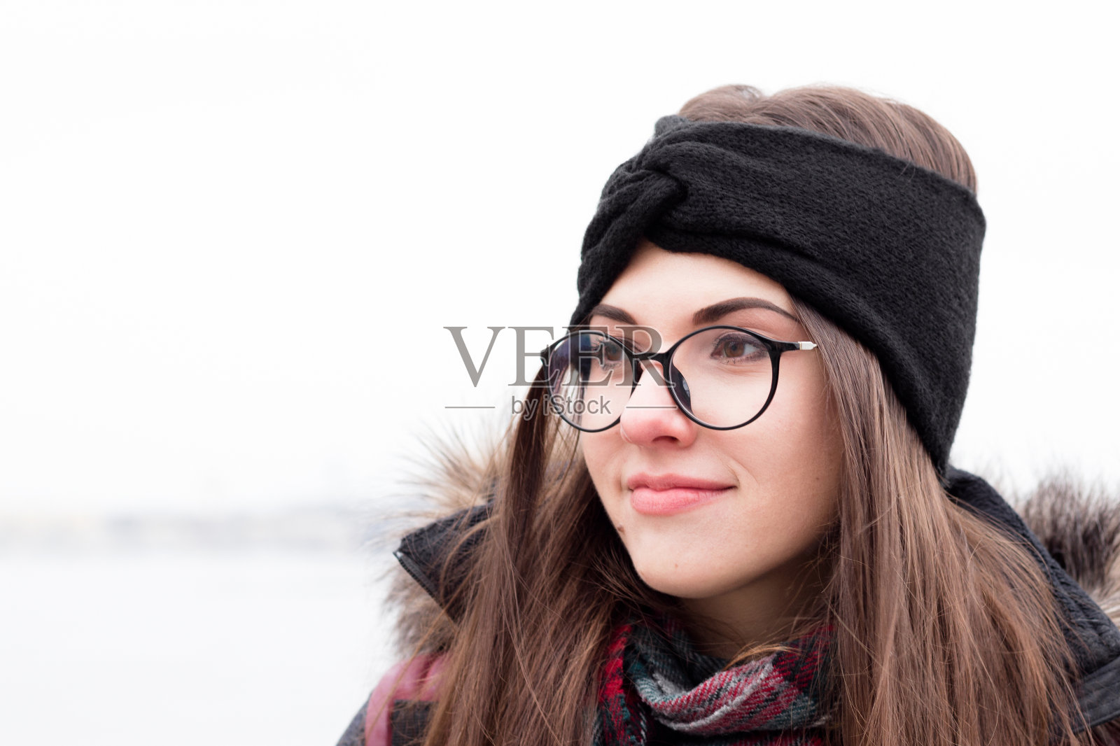 女孩在冬天的衣服，眼镜和温暖的针织头带。一个年轻漂亮的女人的肖像。自然的背景。户外。照片摄影图片