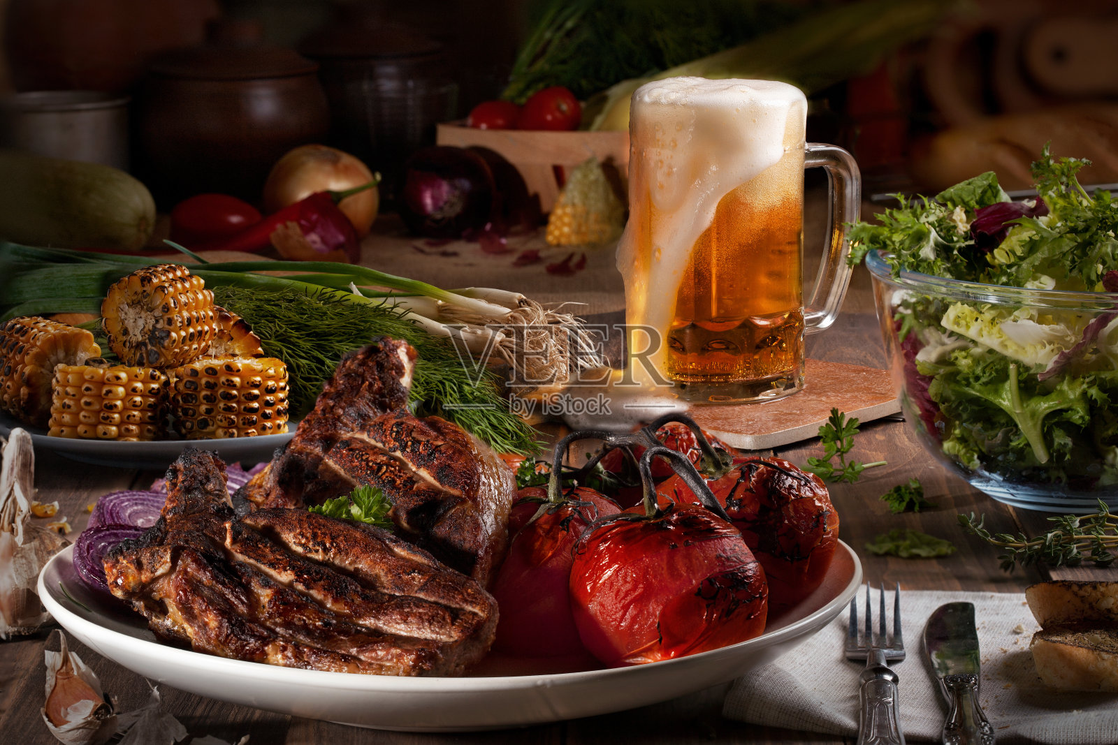 木桌上放着烤肉、西红柿、玉米、青菜、沙拉、鸭肉和大蒜。照片摄影图片
