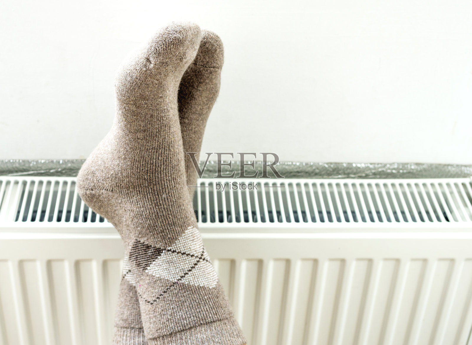 穿着暖和的羊毛袜的男人在暖气散热器的背景上照片摄影图片