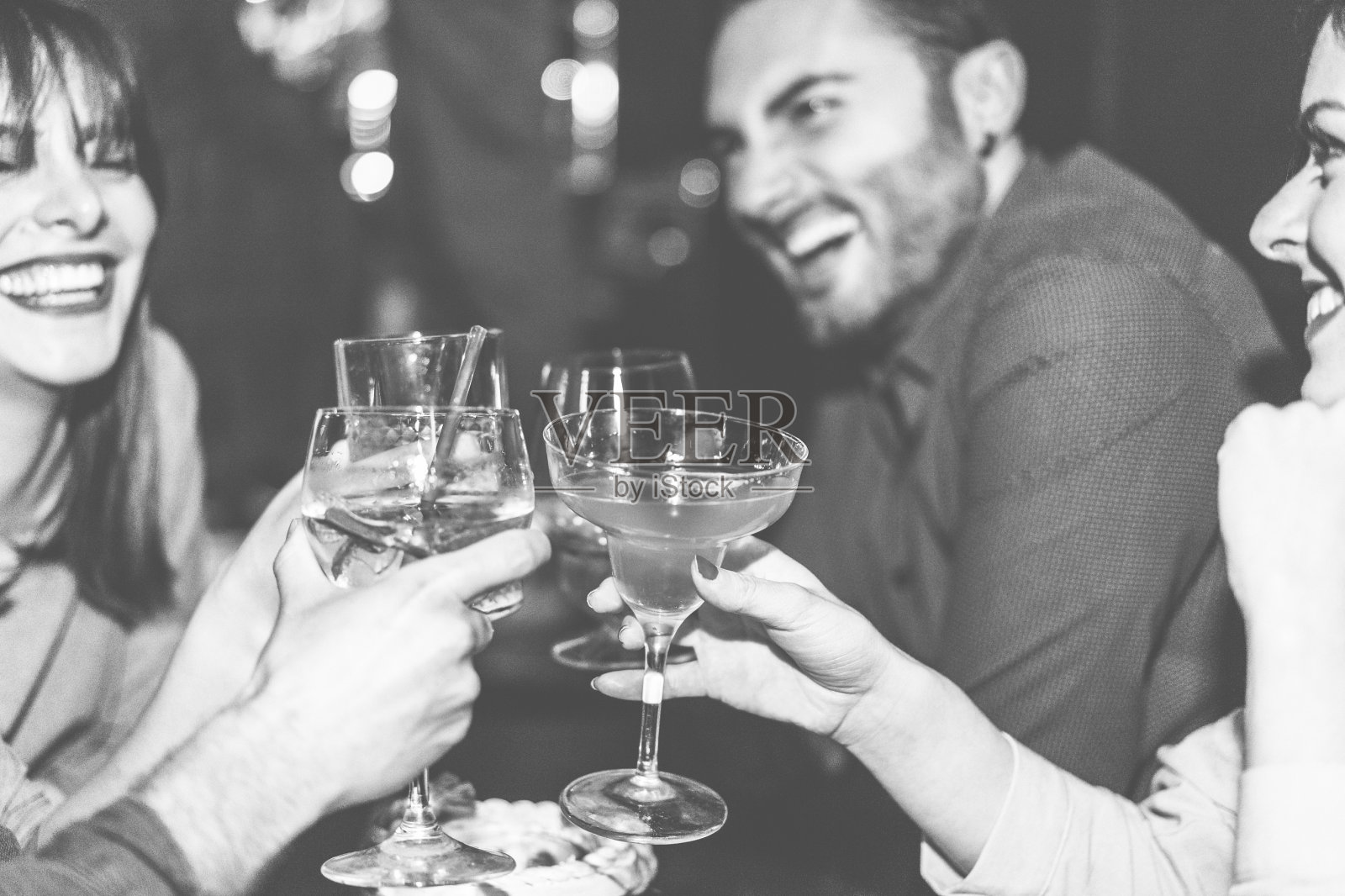 快乐的朋友在鸡尾酒爵士酒吧欢呼-年轻时尚的人有乐趣喝酒和大笑-派对概念-关注右女人手玻璃-黑白编辑-温暖的滤镜照片摄影图片