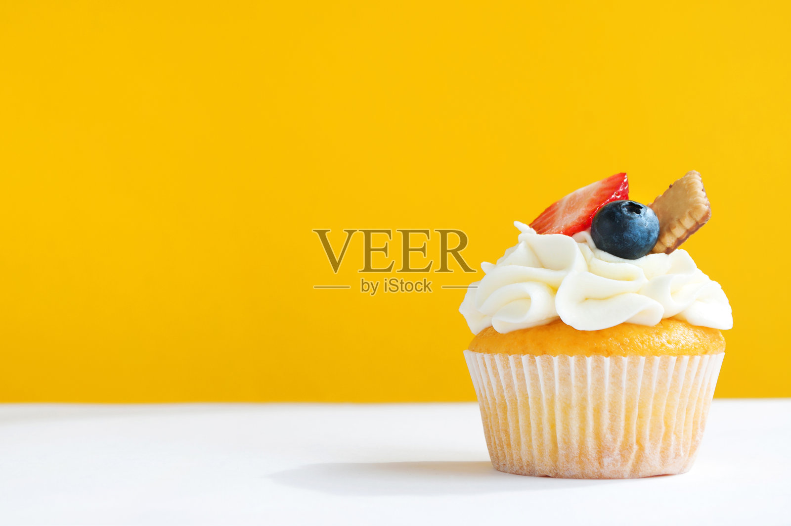 小蛋糕配以鲜奶油、草莓、蓝莓和饼干，背景为黄白色。照片摄影图片