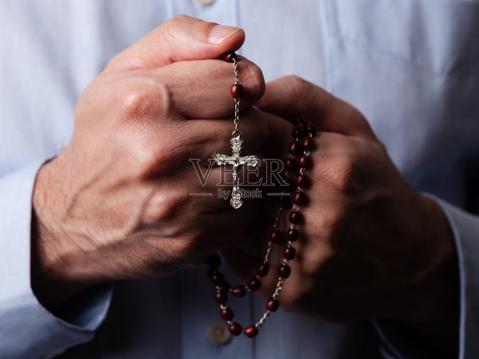 男性手握念珠祈祷，念珠上有耶稣基督在十字架或十字架上的黑色背景。照片摄影图片