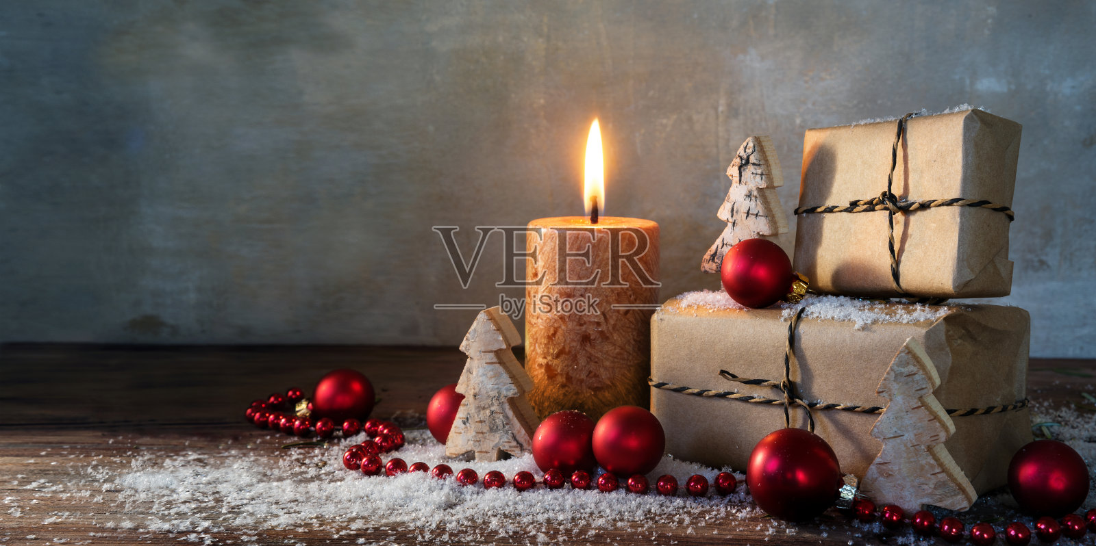 两个礼盒和一个燃烧的蜡烛，红色的圣诞装饰物和小木制玩具树在一些雪地上的乡村木材，复古的背景与大的复制空间，全景格式照片摄影图片