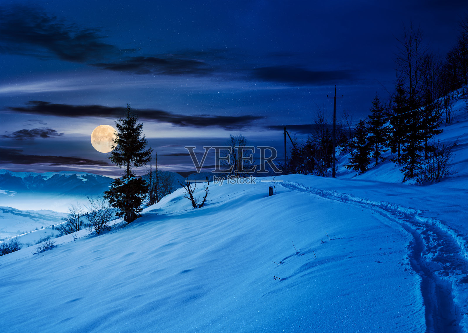 夜晚穿过白雪覆盖的山坡的乡村小径照片摄影图片