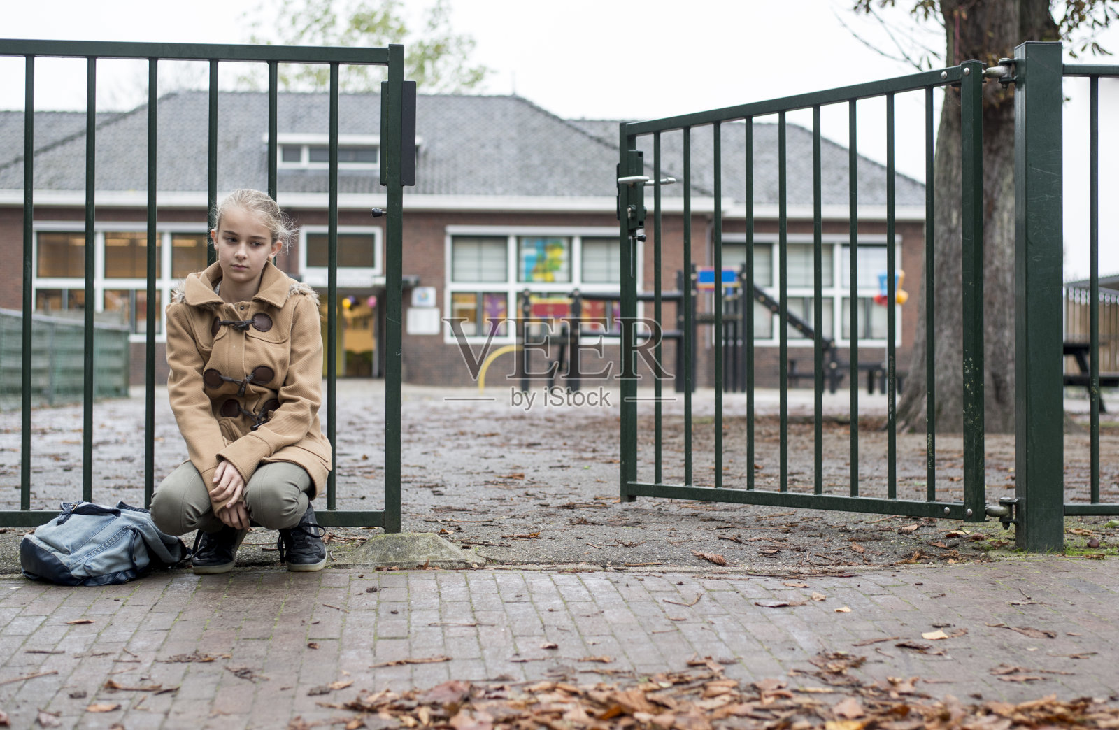悲伤的女孩独自坐在学校门口照片摄影图片
