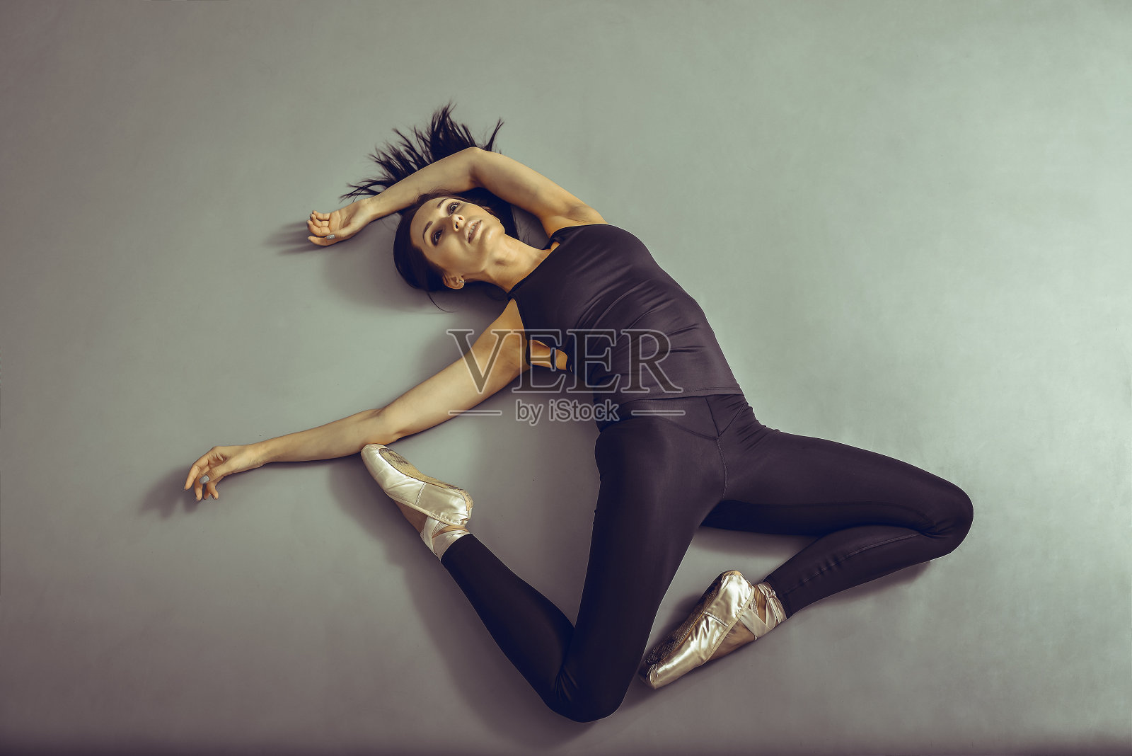 年轻的女芭蕾舞演员躺在芭蕾舞工作室的地板上，没有任何感觉，从上面看。照片摄影图片
