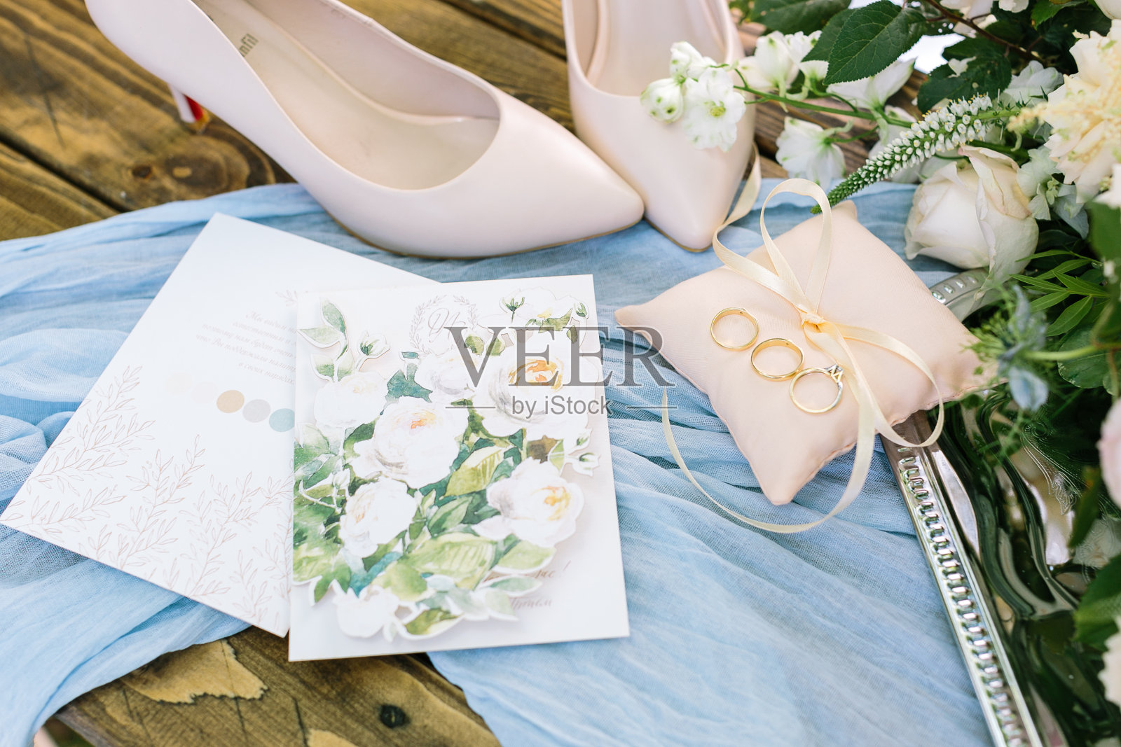风格、婚礼、柔情概念。在铺着浅蓝色窗帘的木桌上，有一个整洁的枕头，上面有金戒指、雅致的尖头鞋和漂亮的明信片照片摄影图片