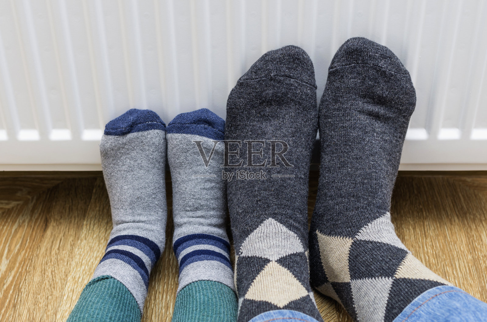 爸爸和儿子穿着冬天的羊毛袜子在家里靠近暖气片。照片摄影图片