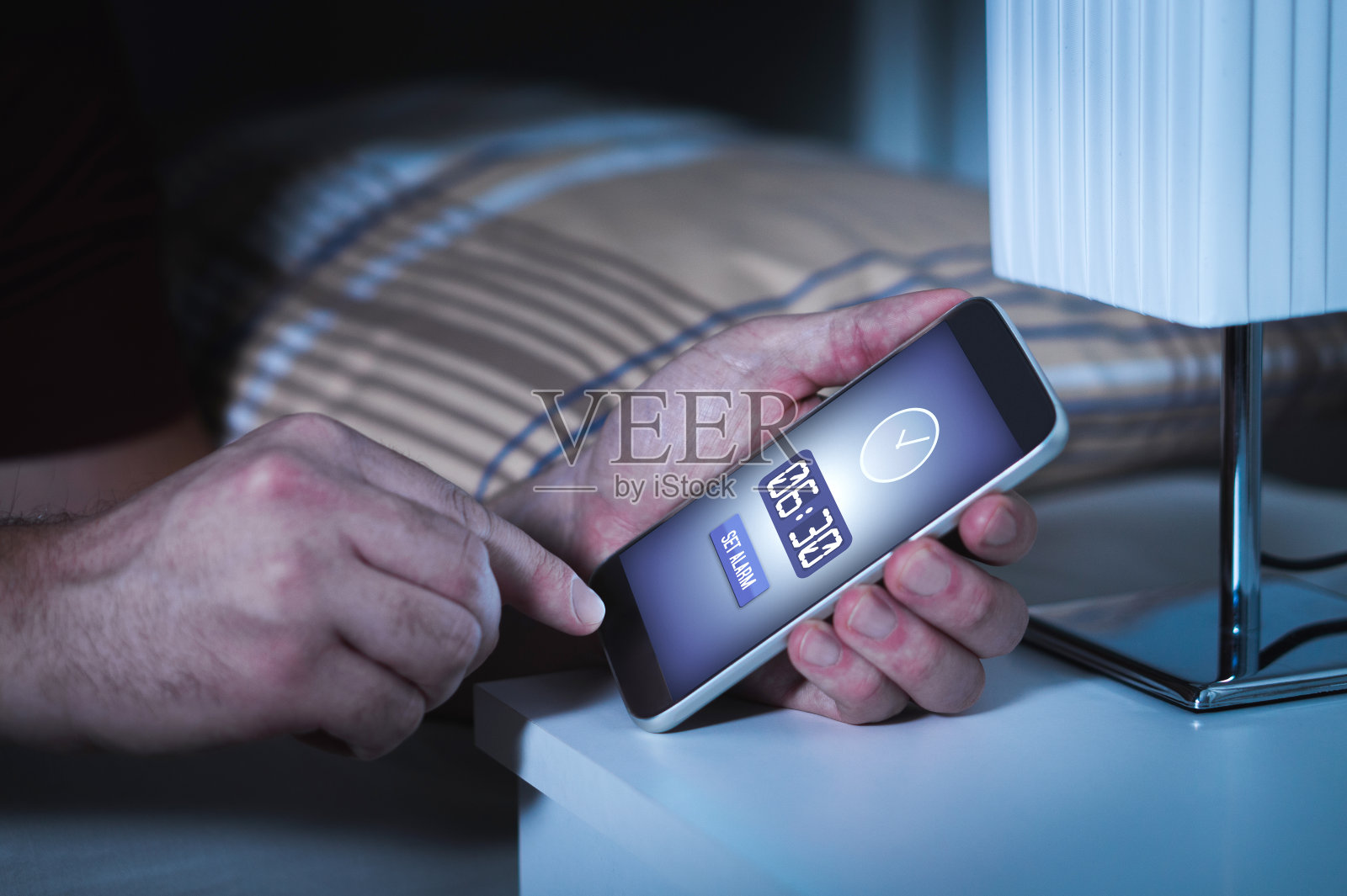 男子在晚上睡觉前用智能手机设定闹钟。手机里的时钟。照片摄影图片