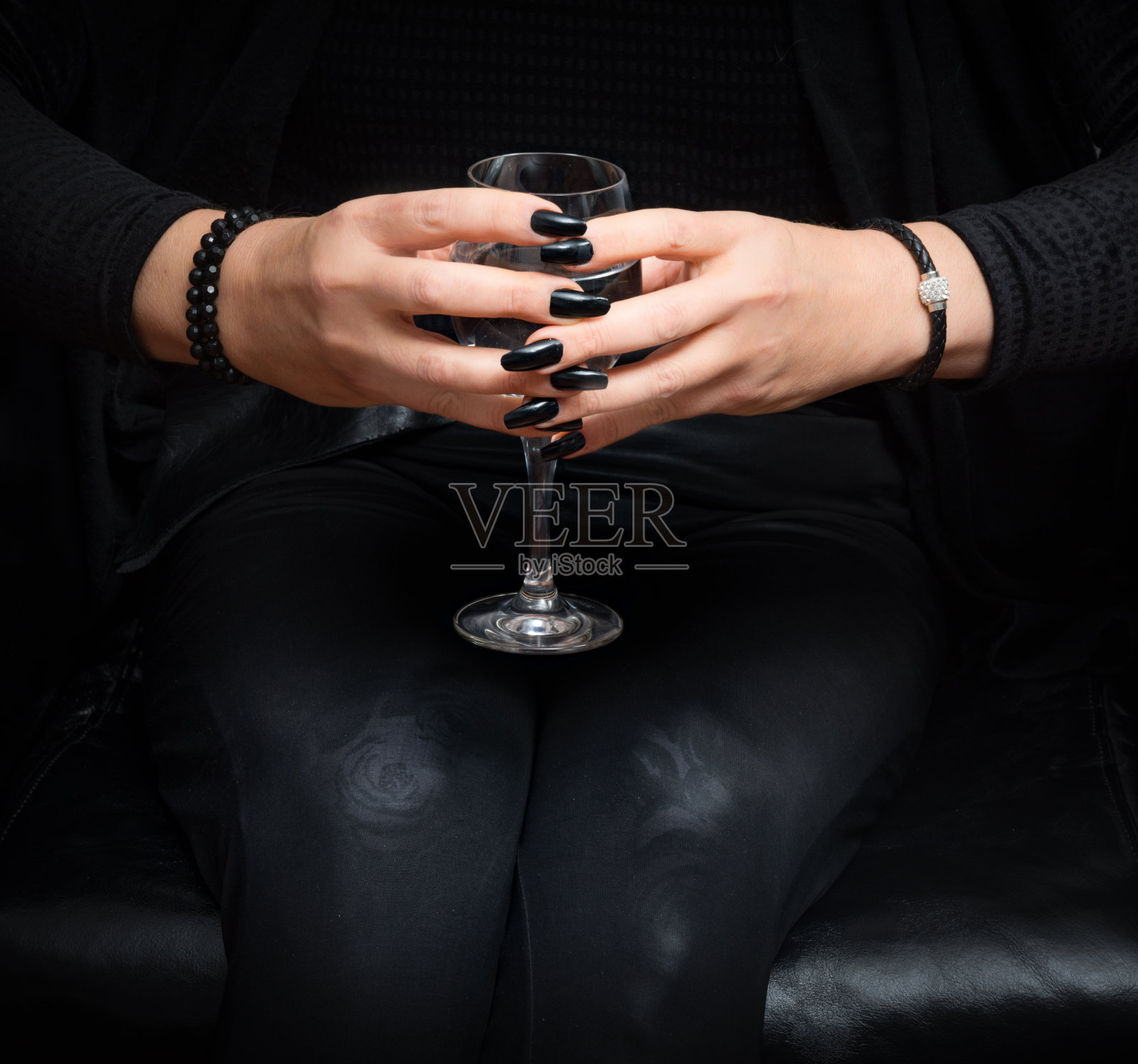 靠近成熟的女人与葡萄酒杯在她的黑色修剪手在黑色扶手椅照片摄影图片