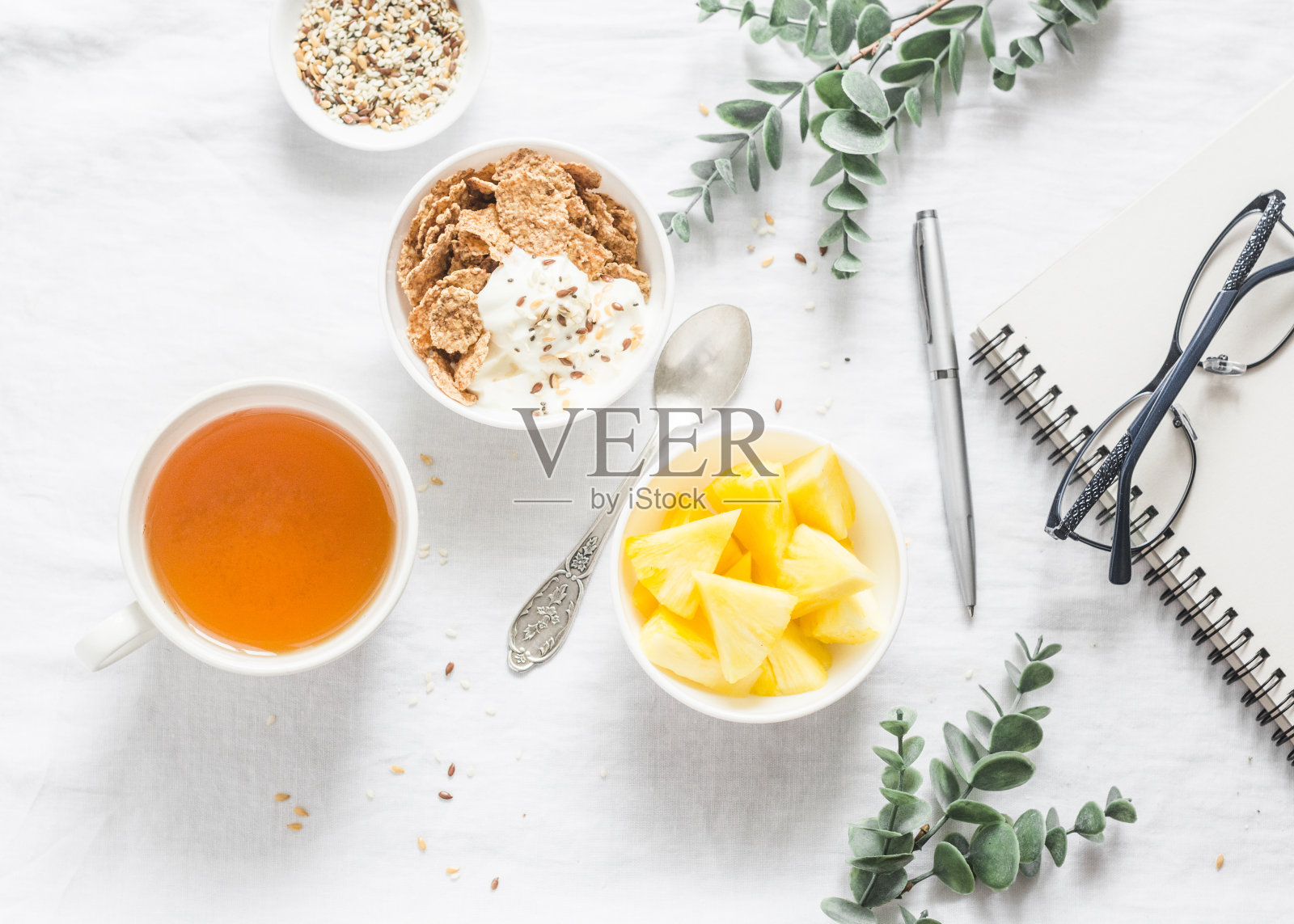 平躺早餐的灵感-希腊酸奶与全谷物，茶，菠萝和记事本，眼镜在一个轻的背景，俯视图照片摄影图片