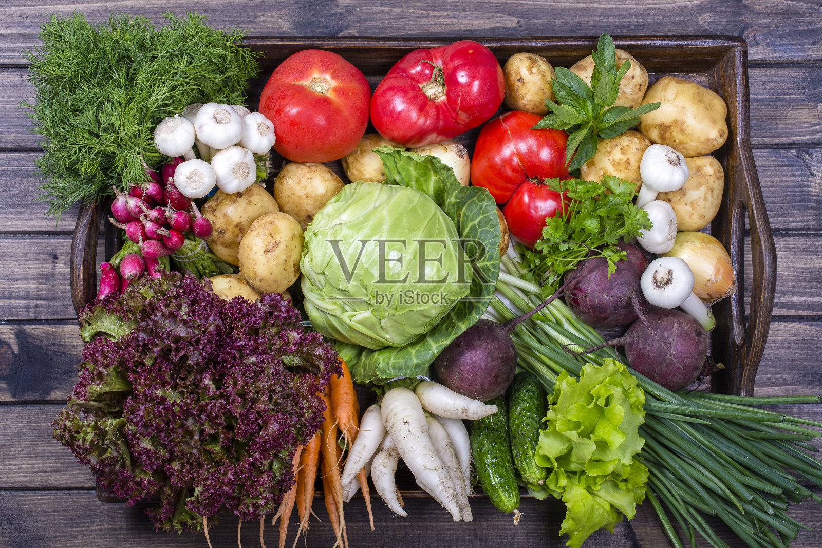 一组新鲜的，生的蔬菜放在质朴的木制餐桌托盘上。选择包括胡萝卜，土豆，黄瓜，番茄，卷心菜，生菜，甜菜根，洋葱，大蒜，萝卜，莳萝和欧芹。俯视图照片摄影图片
