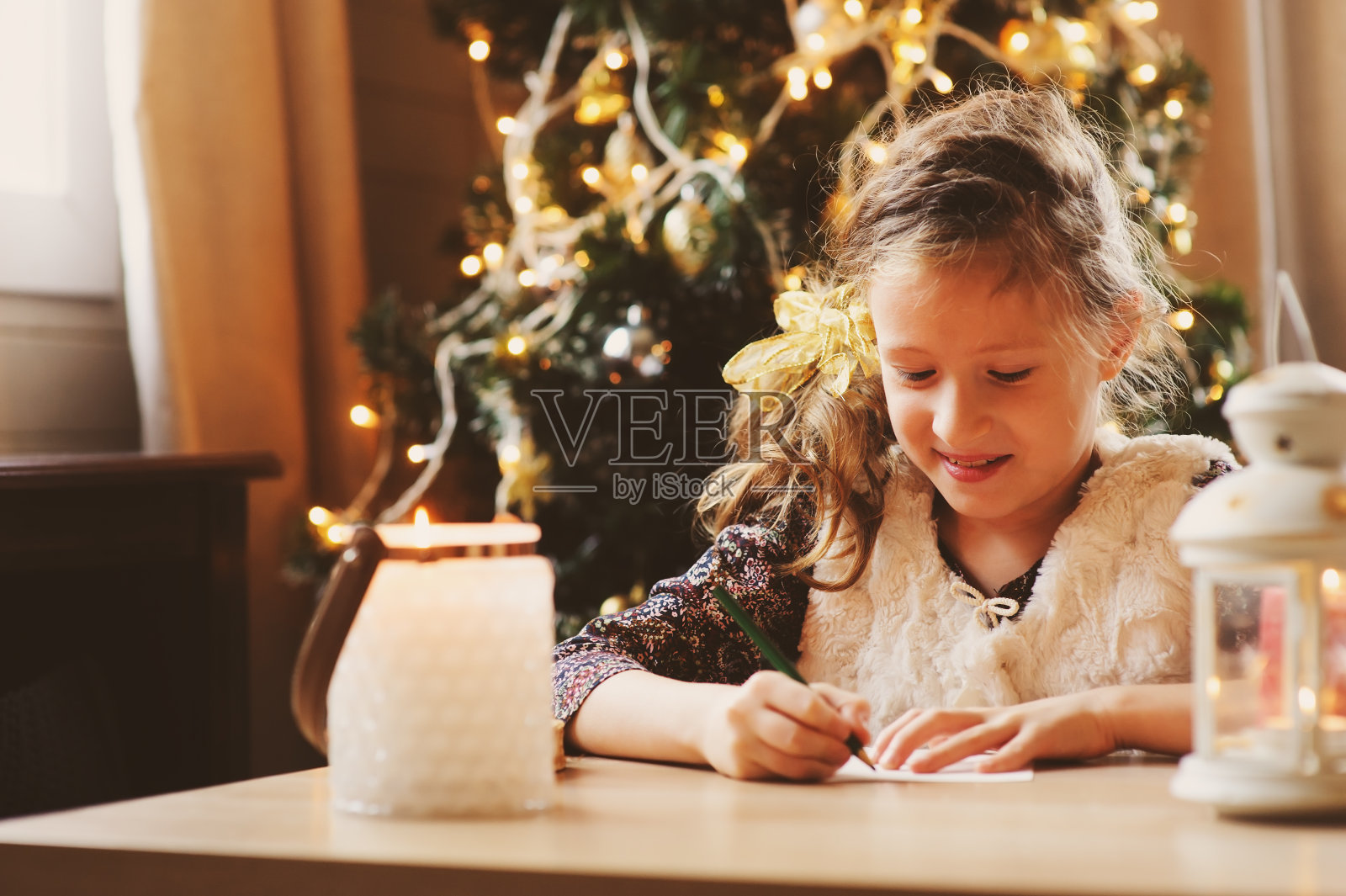 小女孩在家里给圣诞老人写信。8岁的小女孩在家里制作圣诞或新年礼物清单，背景是装饰过的圣诞树照片摄影图片