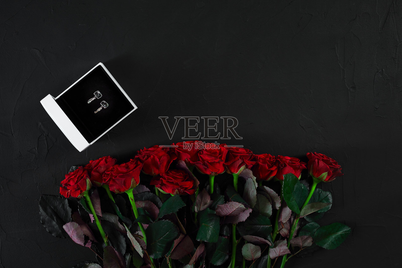 一束红玫瑰和一个带耳环的盒子。视图上照片摄影图片