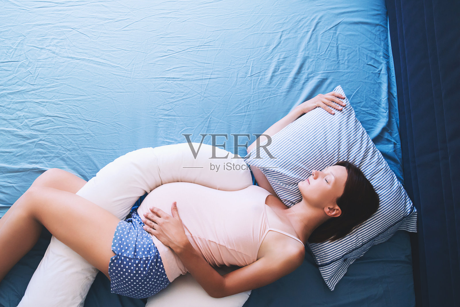 美丽的孕妇放松或睡在床上的肚子支撑枕头。照片摄影图片