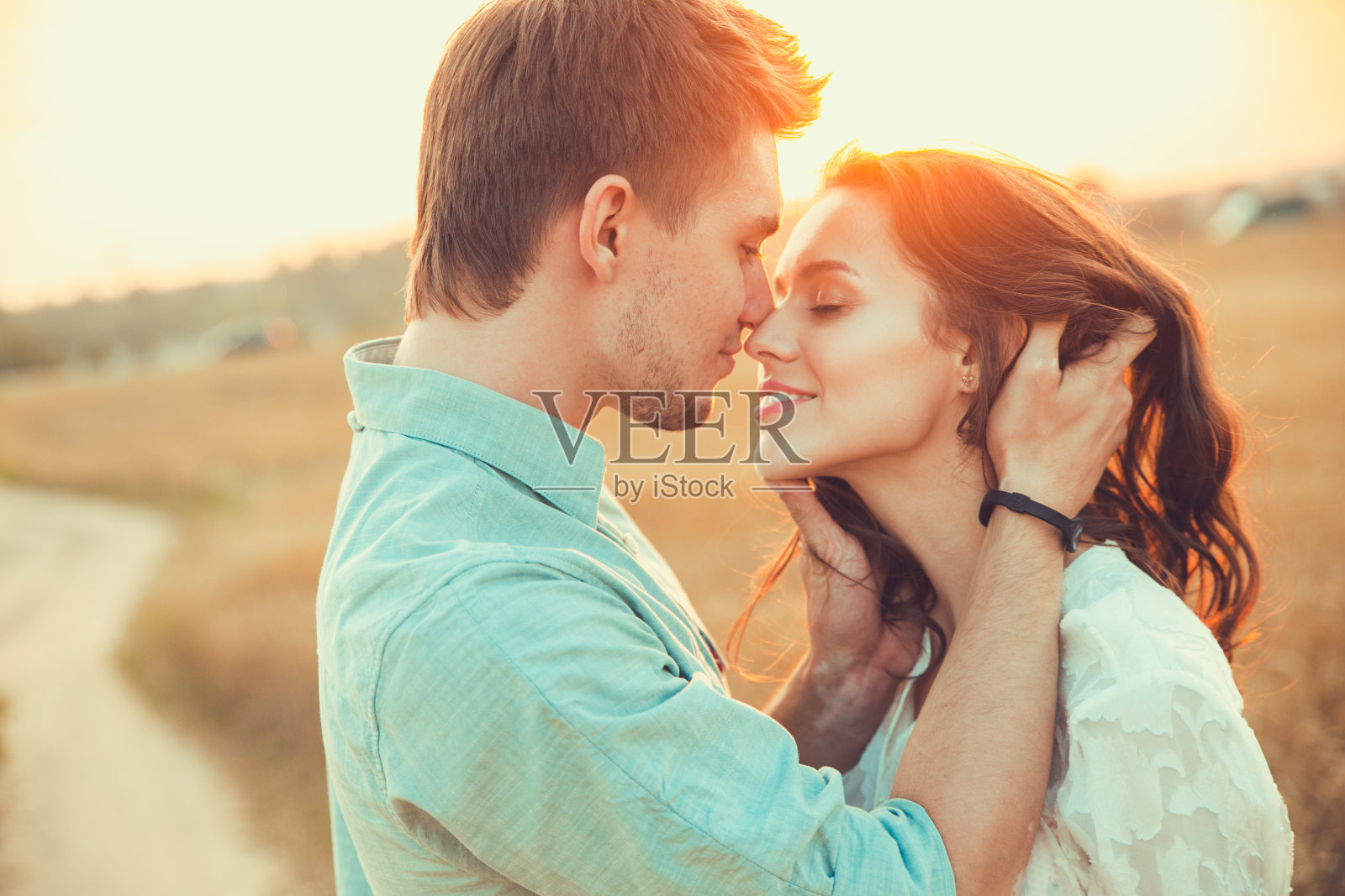 一对在户外相爱的年轻夫妇。在夏天的田野里。两人拥抱。年轻美丽的情侣在日落的田野上停留和亲吻。柔和的阳光的颜色。照片摄影图片